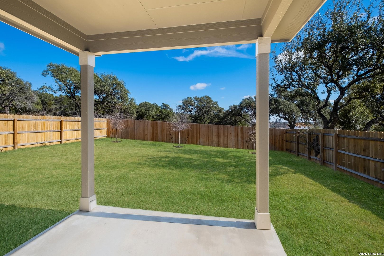 Covered back patio overlooking lush green backyard with oak trees and privacy fence in Bricewood, San Antonio, Texas