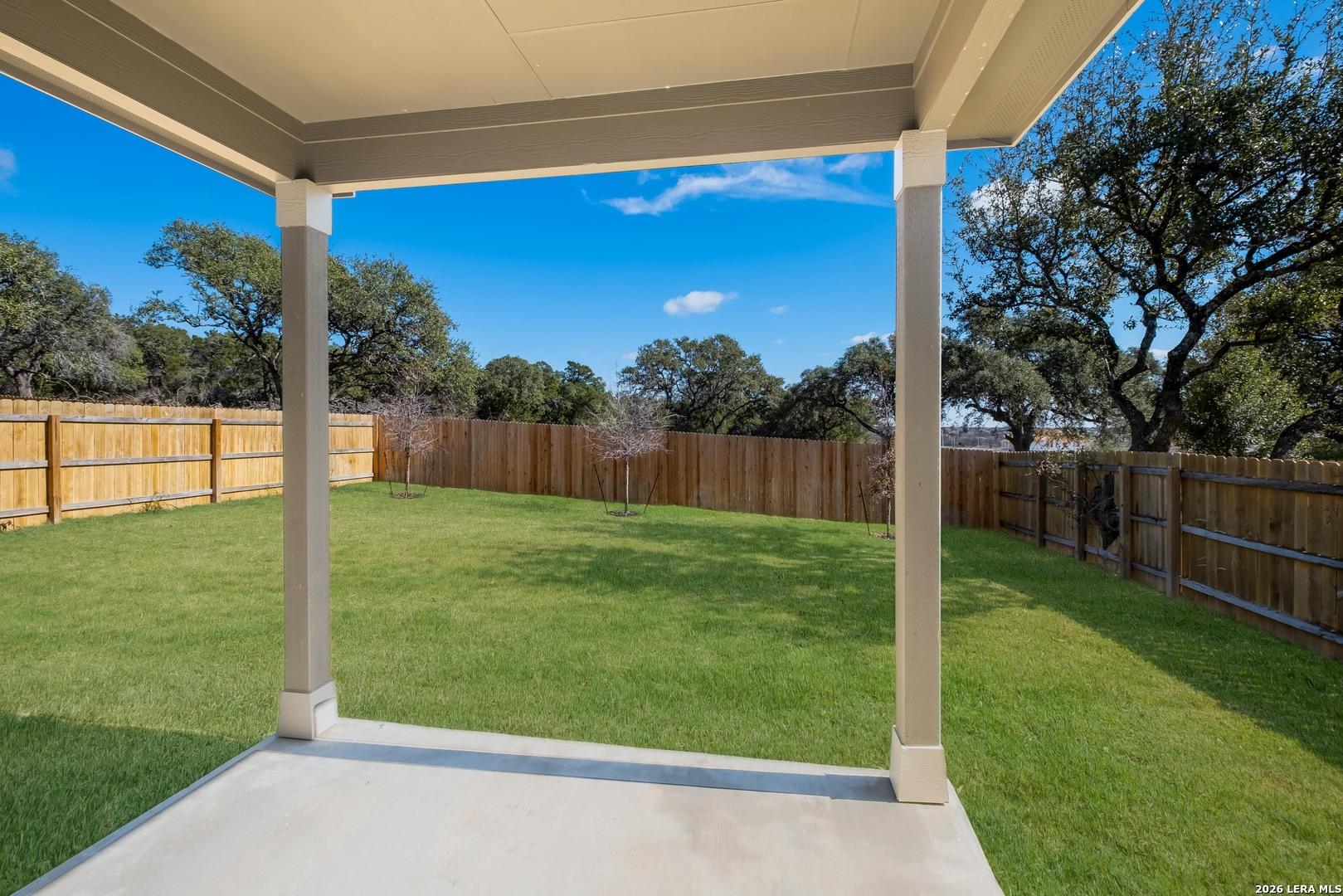 Covered back patio overlooking lush green backyard with oak trees and privacy fence in Bricewood, San Antonio, Texas