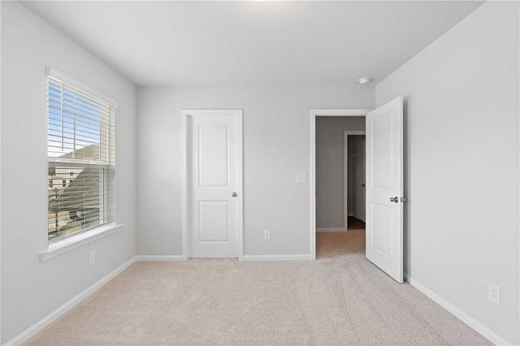 Bright empty bedroom with neutral walls, beige carpet, window blinds, and double doors in Davidson Homes The Hickory B, Winder, GA