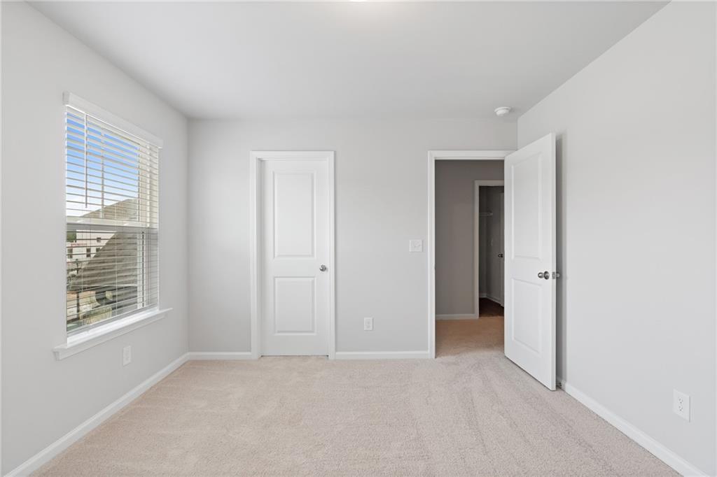 Bright secondary bedroom with beige carpet, white walls, window blinds, and closet door in Davidson Homes The Hickory A, Winder, GA