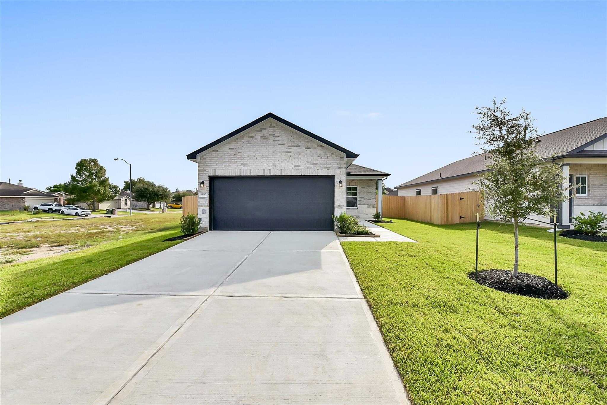 Modern white brick 1-story home with 2-car garage, driveway, and green lawn in The Villages at WestPointe, Dayton, Texas