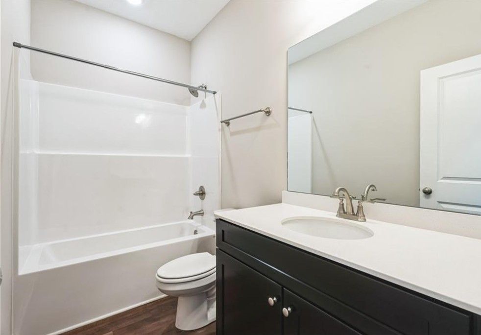 Modern bathroom with white tub-shower combo, black vanity, and mirror in Evermore Homes The Aurora A, Cusseta, Alabama