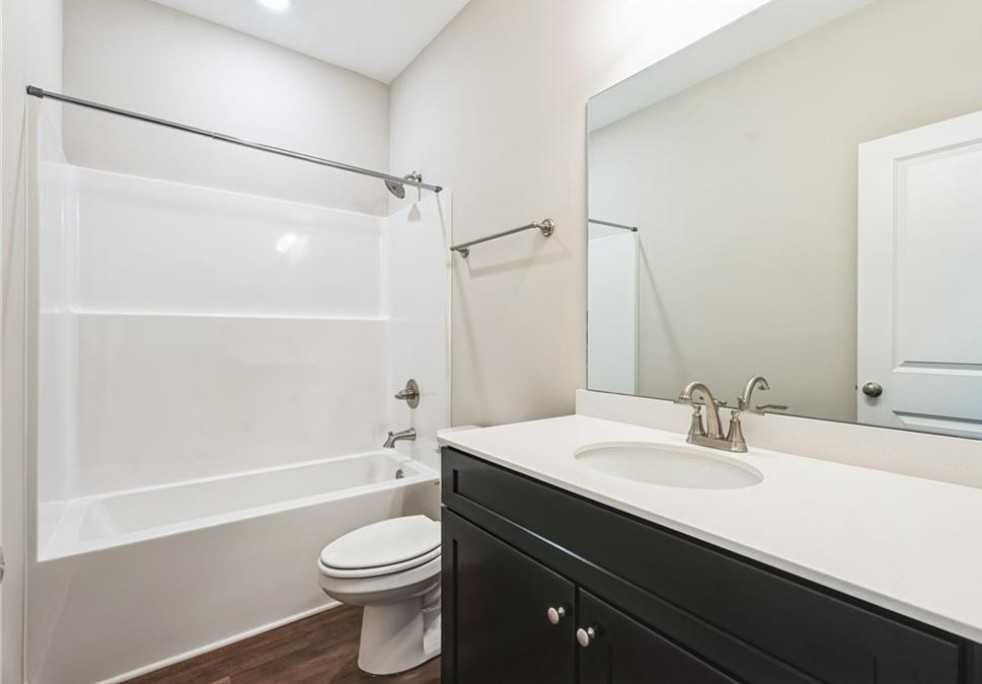 Modern bathroom with white tub-shower combo, black vanity, and mirror in Evermore Homes The Aurora A, Cusseta, Alabama