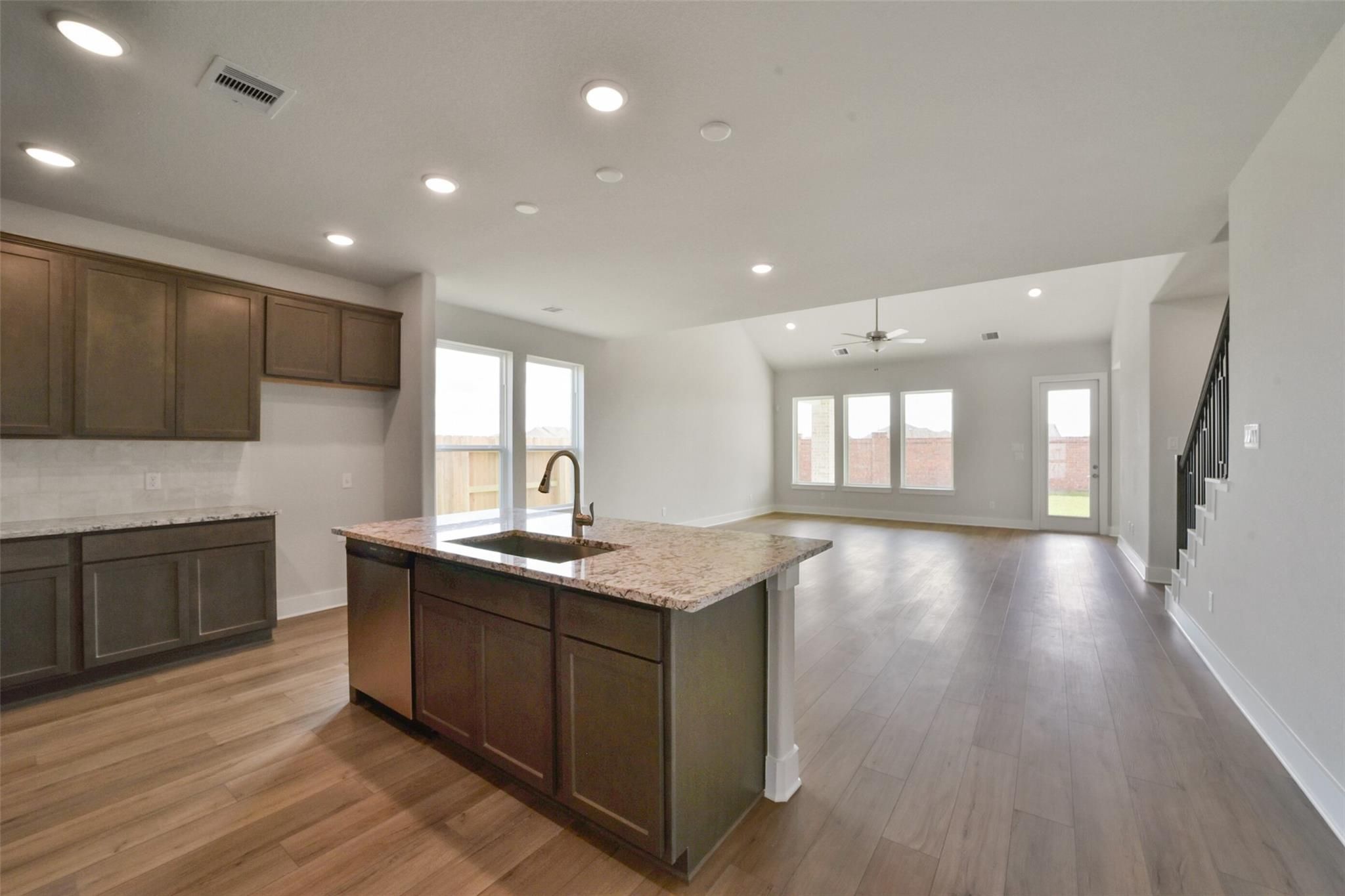 Modern open-concept kitchen with brown cabinets, granite island sink, hardwood floors, and large windows in Davidson Homes The Zion A, Lago Mar