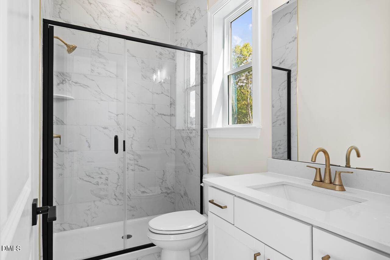 Elegant marble-tiled bathroom with glass walk-in shower, gold fixtures, and white vanity in Davidson Homes' Crawford D, Wake Forest, NC