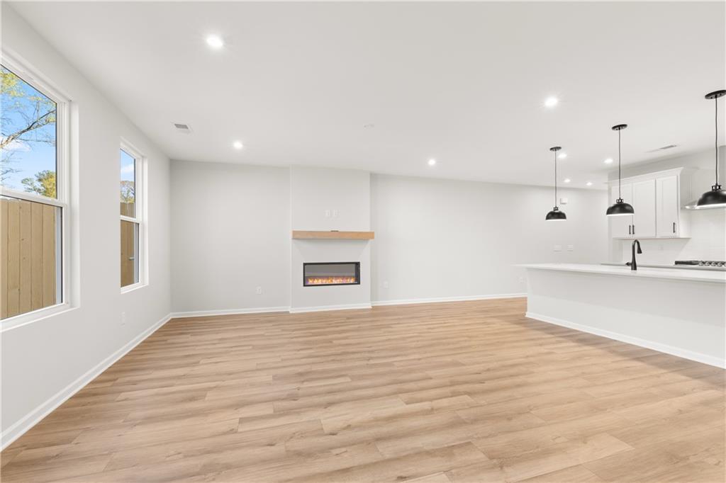 Modern open living room with gas fireplace, hardwood floors, and white kitchen island in Davidson Homes The Cary A, Winder, Georgia