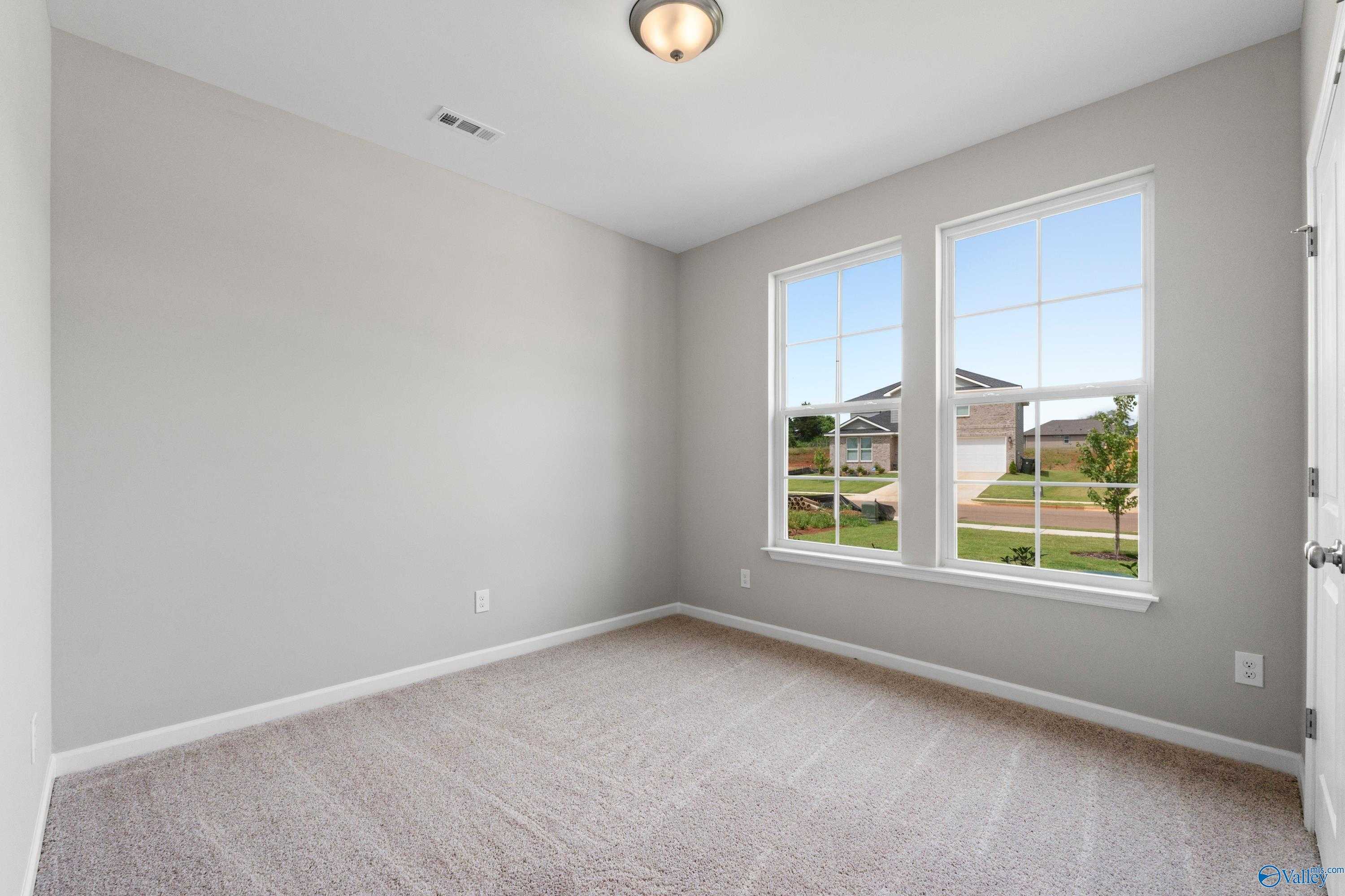 Bright bedroom with light gray walls, beige carpet, and large windows overlooking neighborhood in The Aurora home, Harvest, Alabama