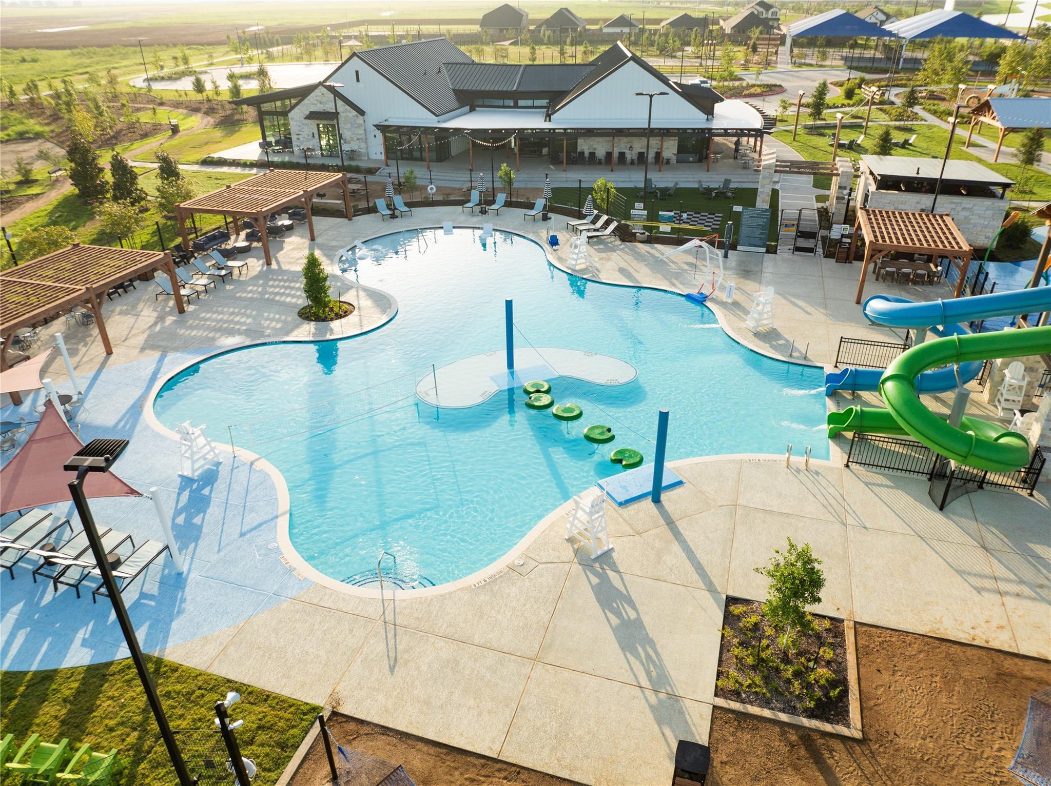 Resort-style community pool with green water slide, lily pads, lounge chairs and cabanas in Emberly, Beasley, Texas