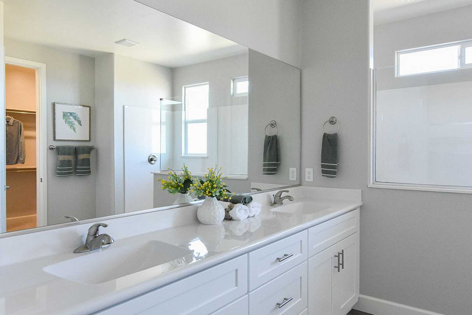 Spacious master bathroom in The Summit B with double vanity, large mirrors, gray walls, and walk-in closet access