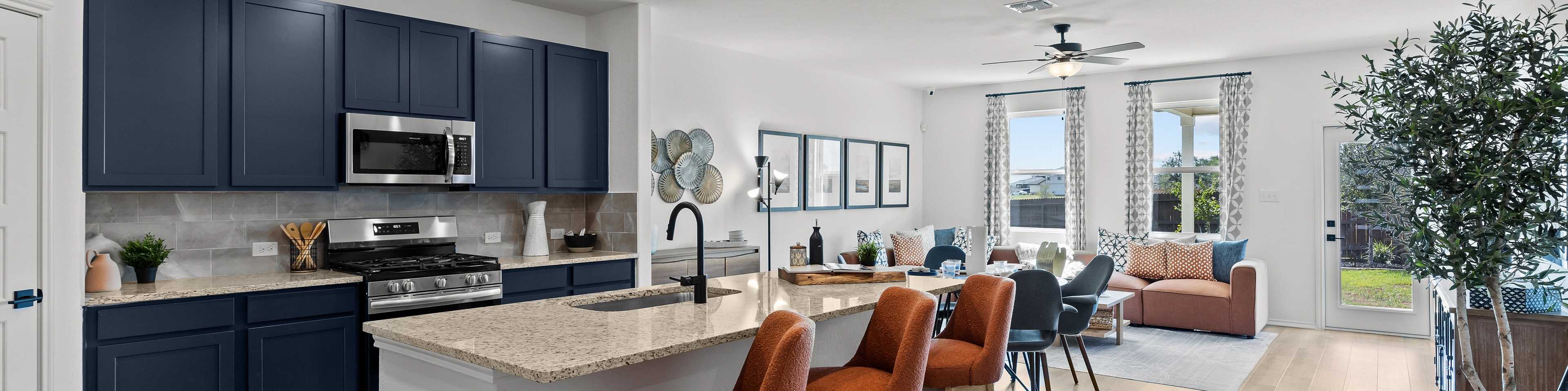 Modern open-concept kitchen and living area in new Elmendorf home with navy cabinets, granite island, orange stools