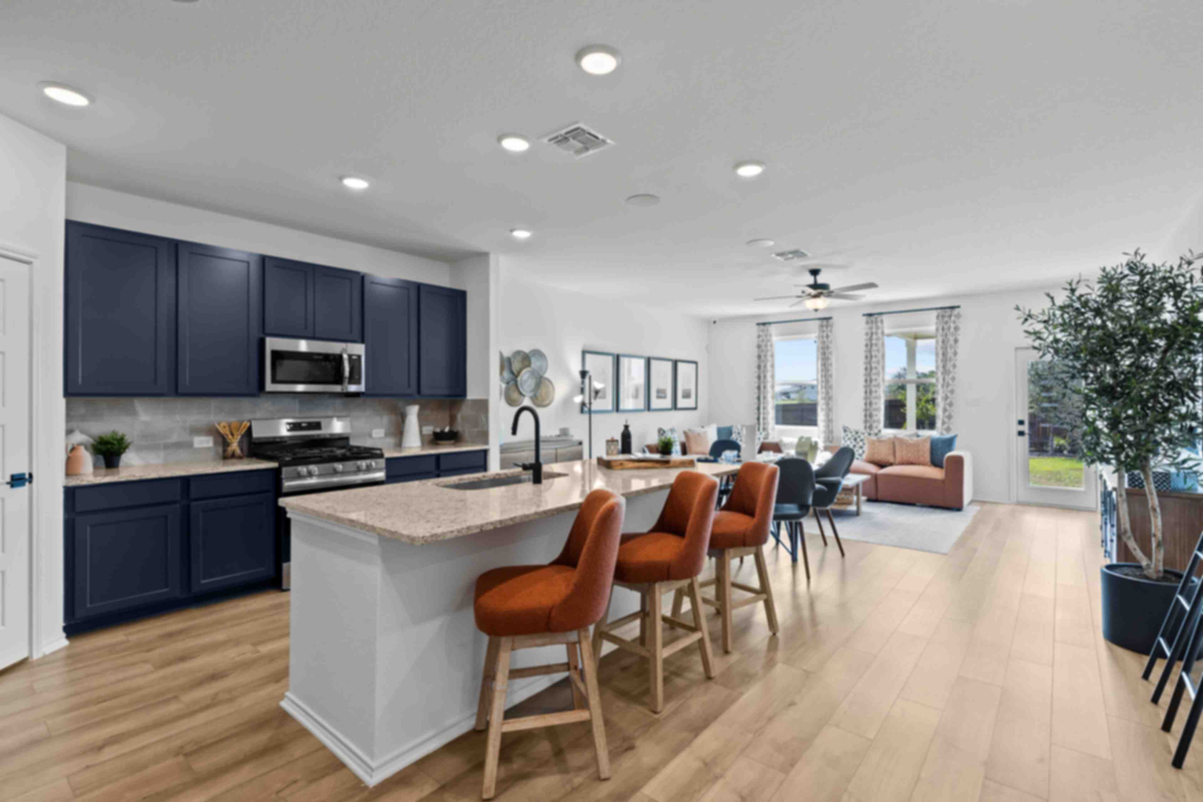 Open-concept kitchen living area at Hickory Ridge in Elmendorf Texas with navy cabinets quartz island and orange seating