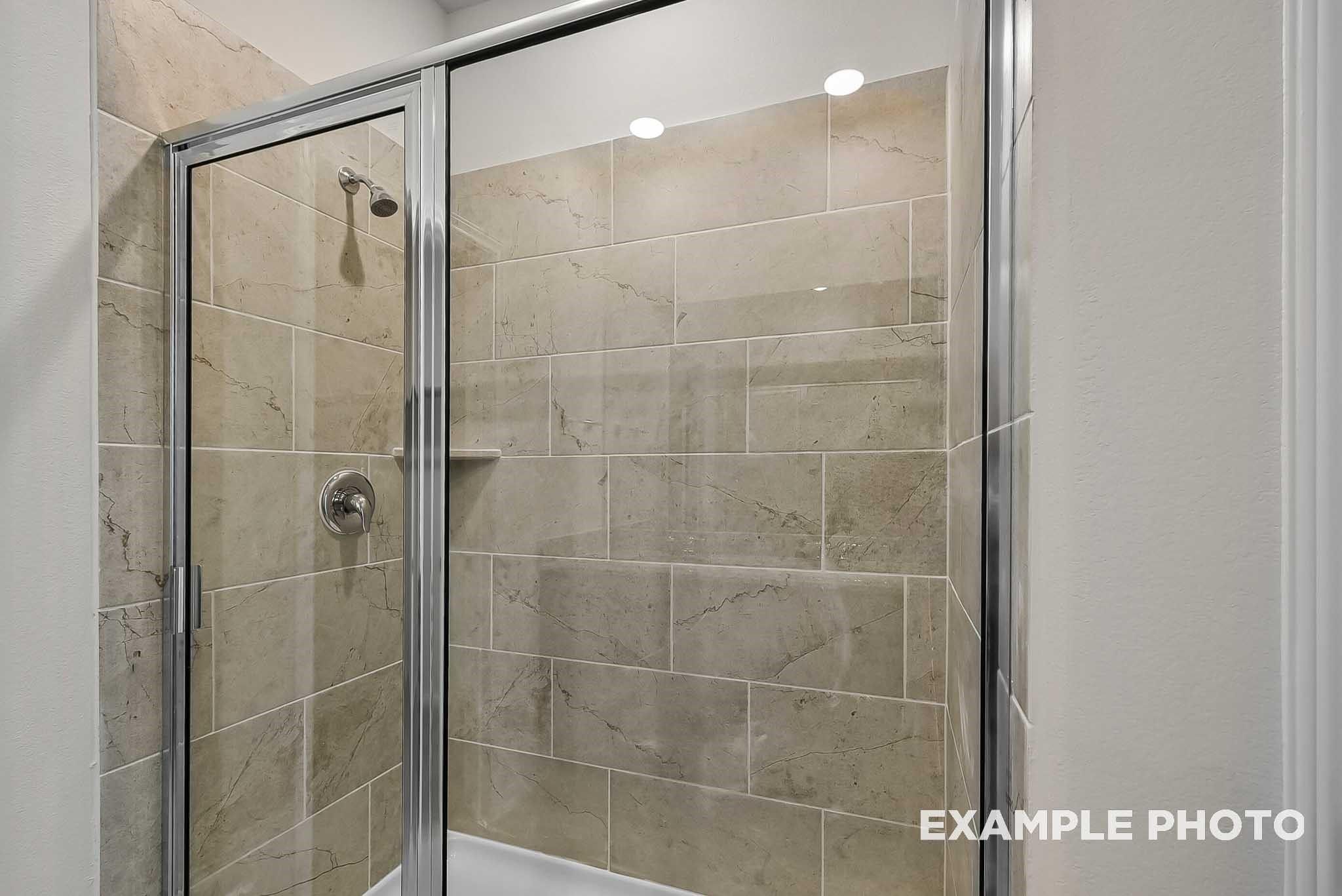 Modern walk-in shower with beige tile surround in The Blanco F floor plan at Spring Branch Crossing, Conroe, Texas.