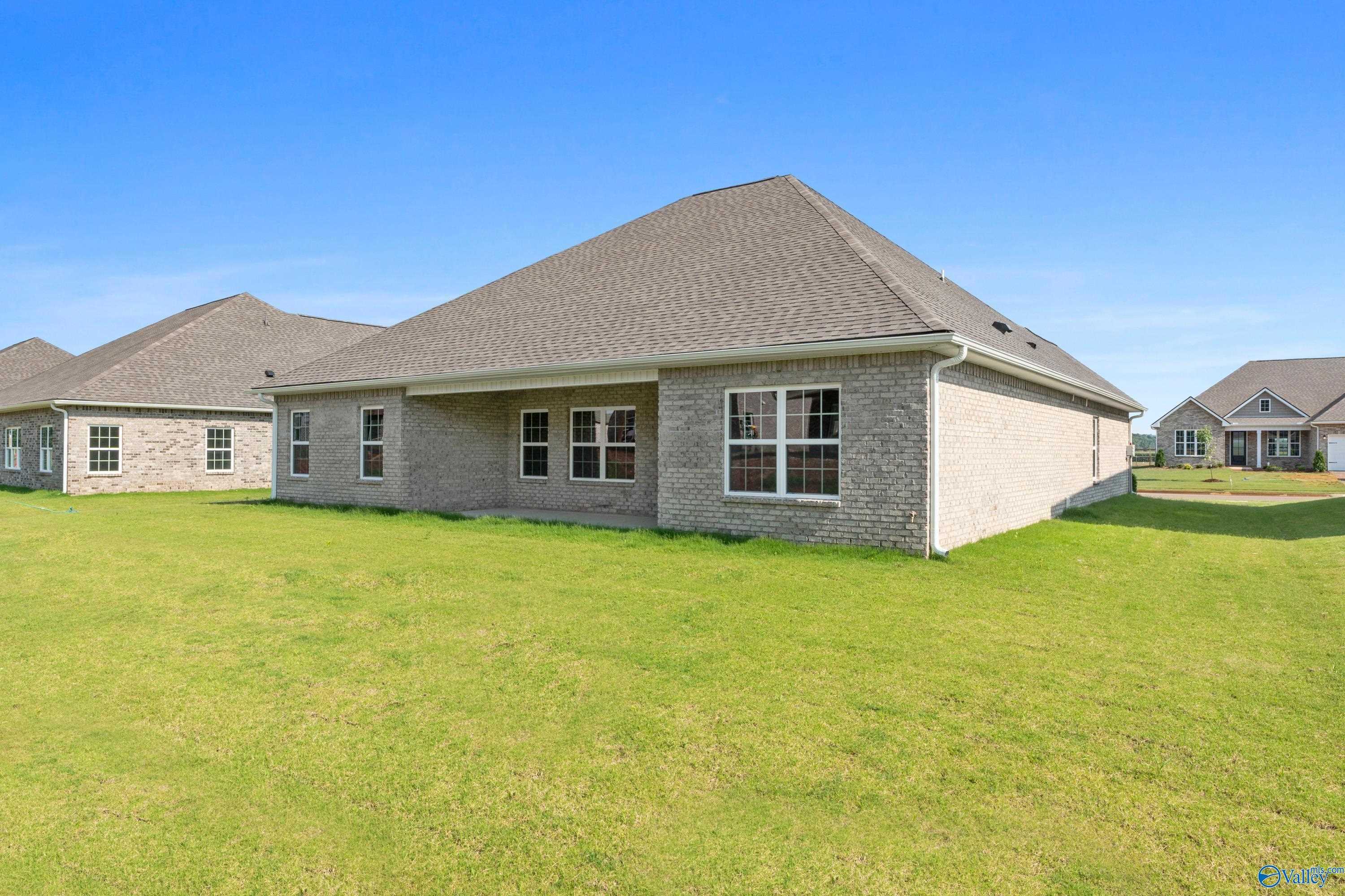 Brick single-story home with gabled roof, large windows, and 3-car garage on lush green lawn in Kendall Farms, Toney, Alabama