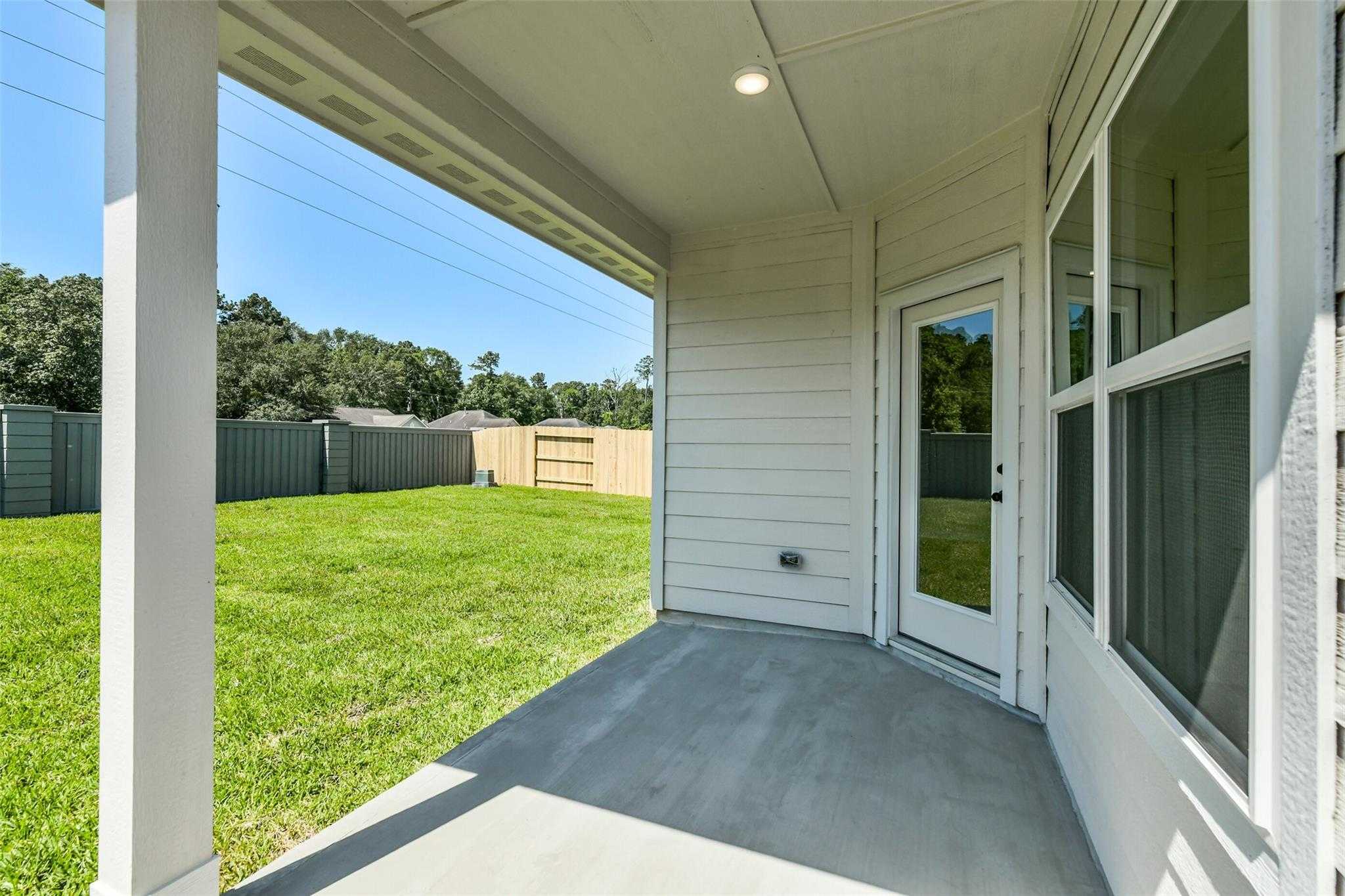 Covered back patio with glass doors, concrete flooring, and lush green lawn in Davidson Homes The Daphne H, Sundance Cove, Crosby, Texas