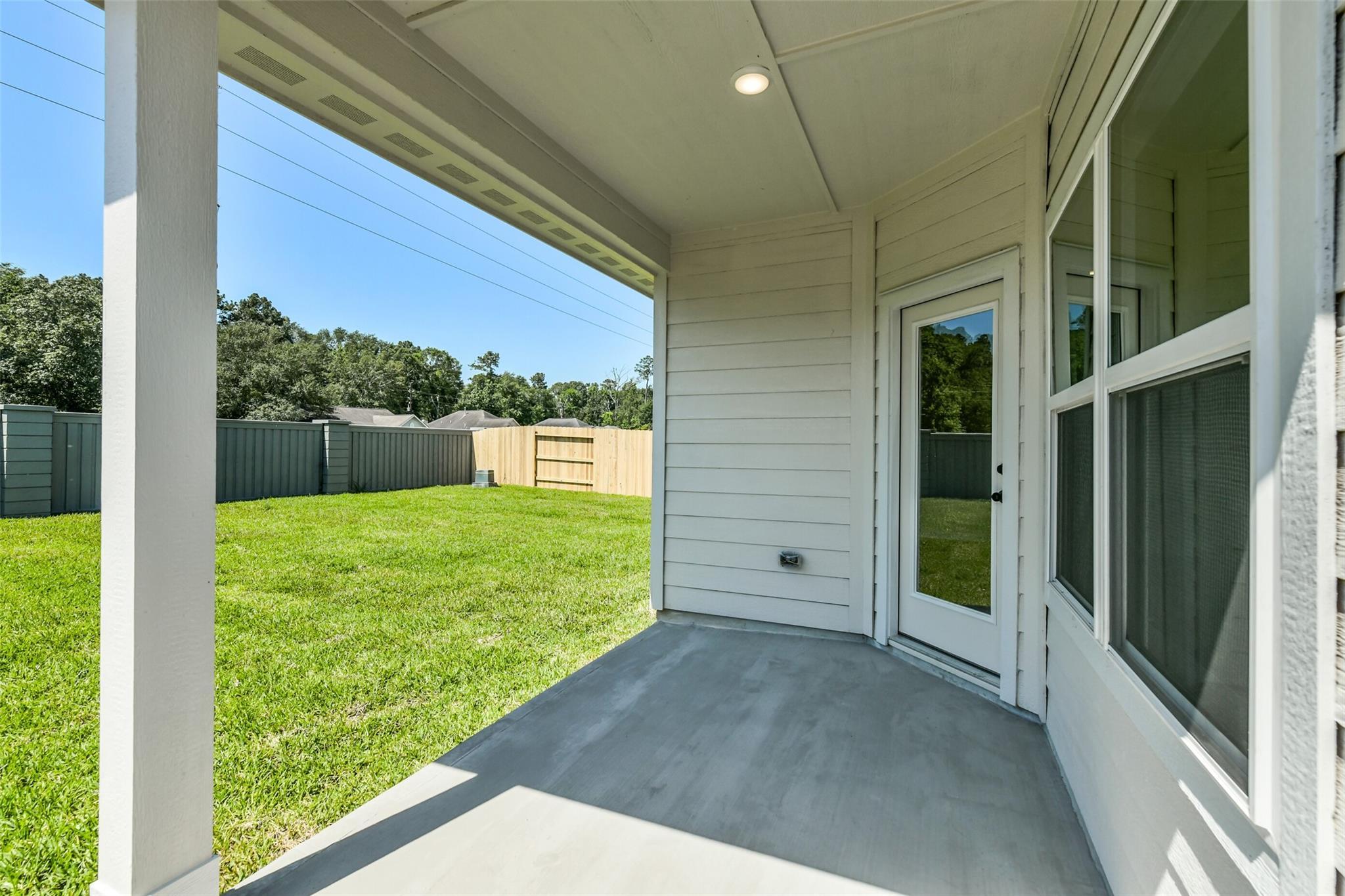 Covered back patio with glass doors, concrete flooring, and lush green lawn in Davidson Homes The Daphne H, Sundance Cove, Crosby, Texas