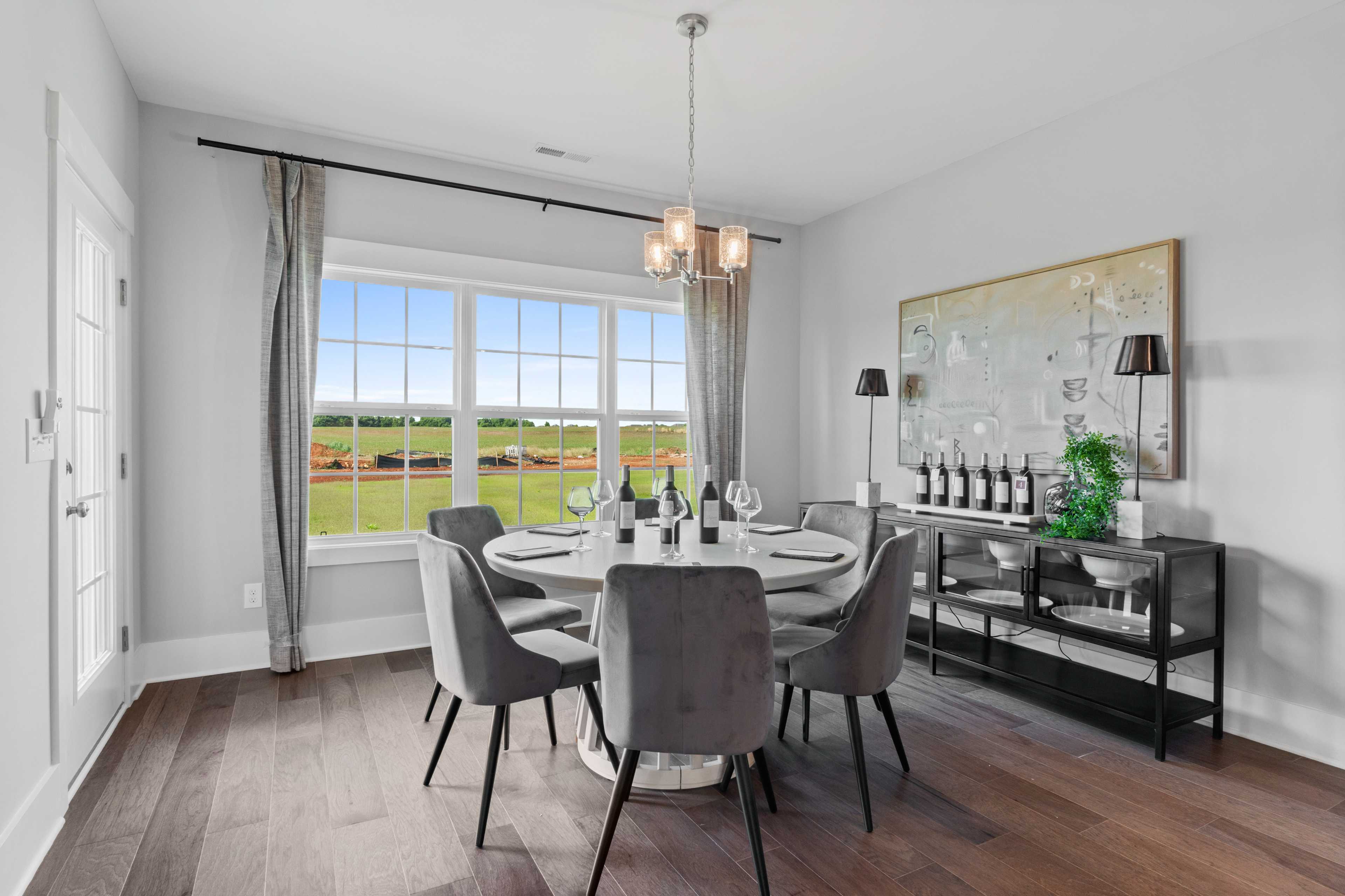 Spacious dining room in Creekside home, Harvest Alabama with round table, gray velvet chairs, chandelier, and golf course view