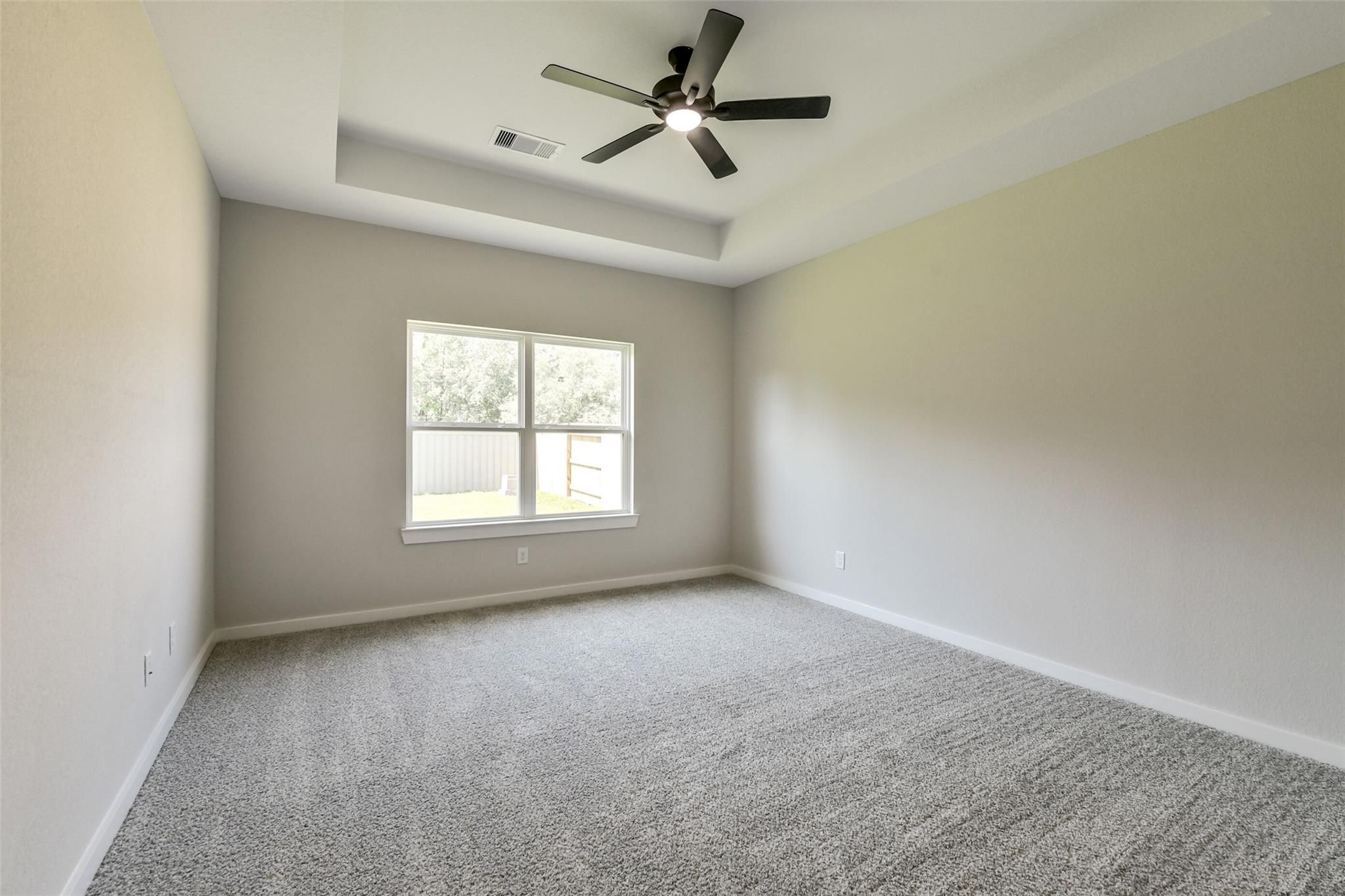 Spacious bedroom with tray ceiling, dual fans, beige walls, and large windows in Davidson Homes The Daphne H, Crosby, Texas