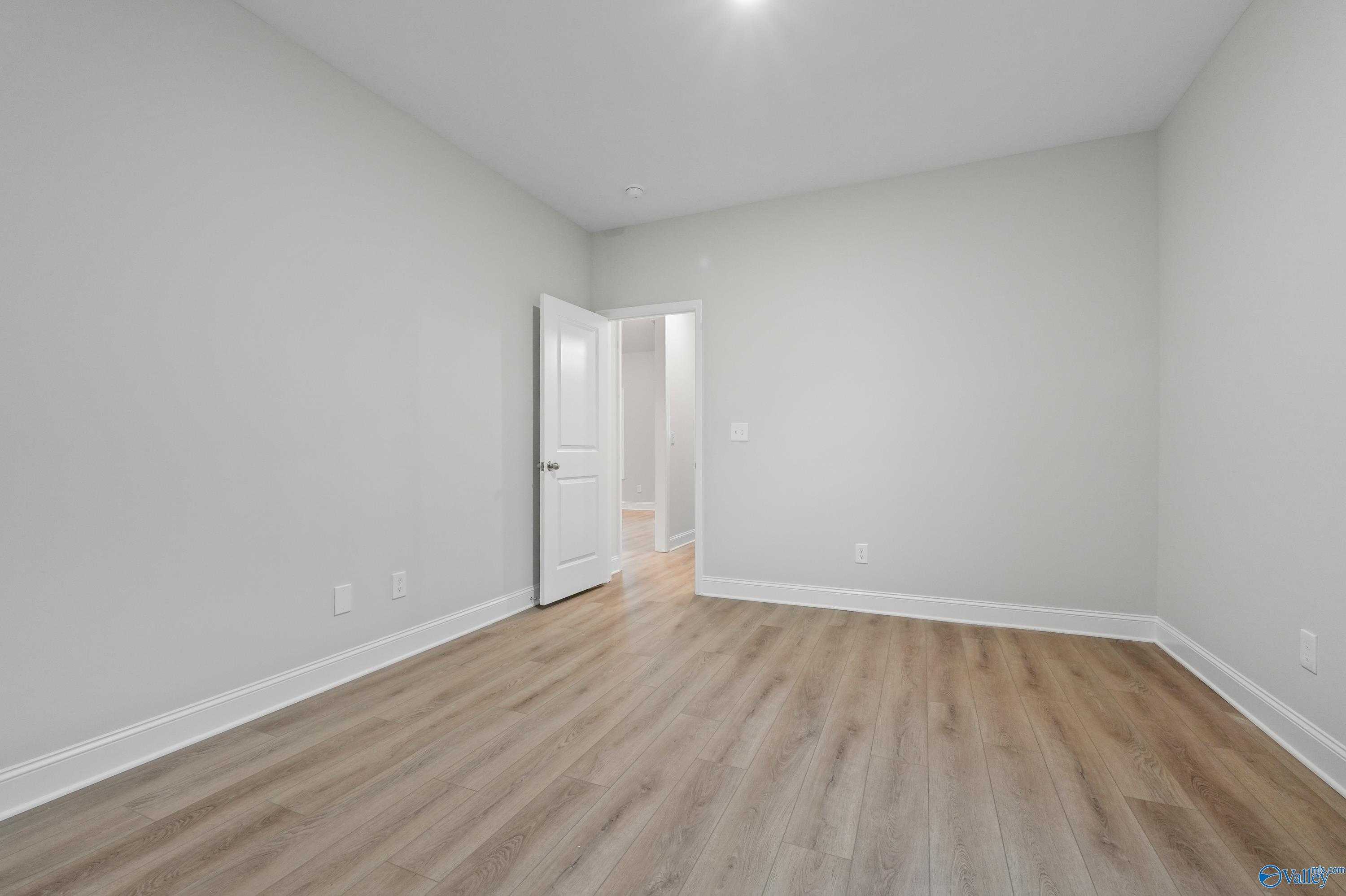 Empty bedroom with light gray walls, hardwood floors, and open door in Davidson Homes The Lanier, Creekside, Harvest, Alabama