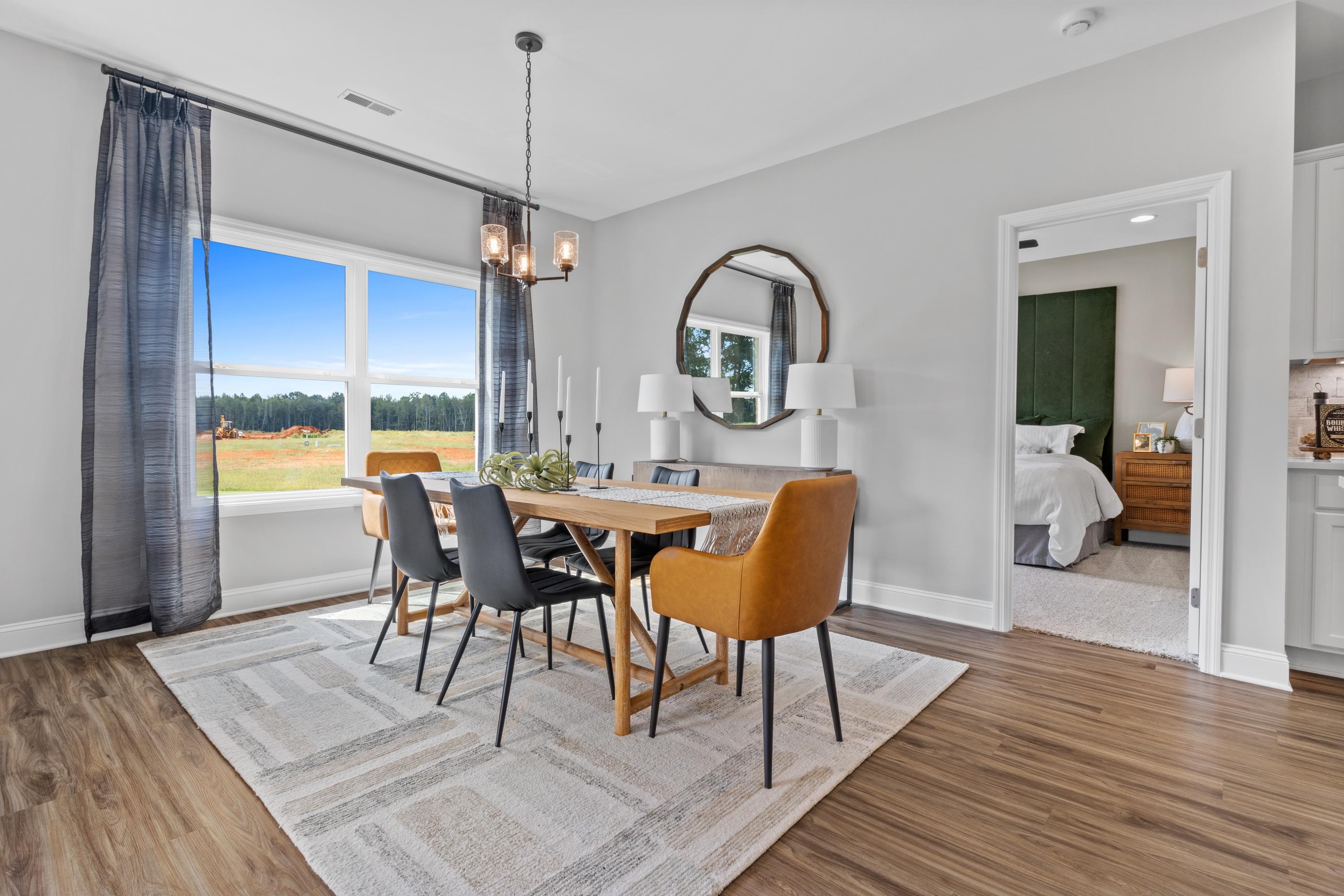 Spacious dining room in Wood Trail Toney Alabama with wooden table, orange chairs, round mirror, chandelier, and field views through large windows