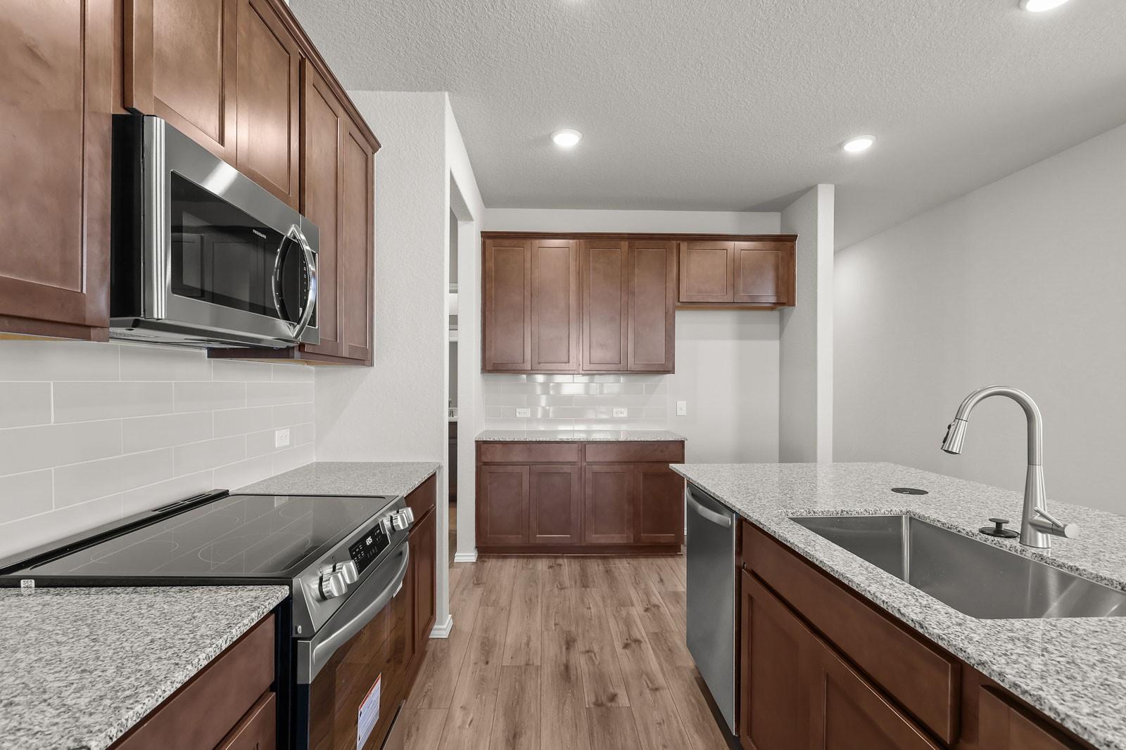 Modern kitchen with granite countertops, stainless appliances, and wood cabinetry in The Frio G floor plan at Heartland, TX.