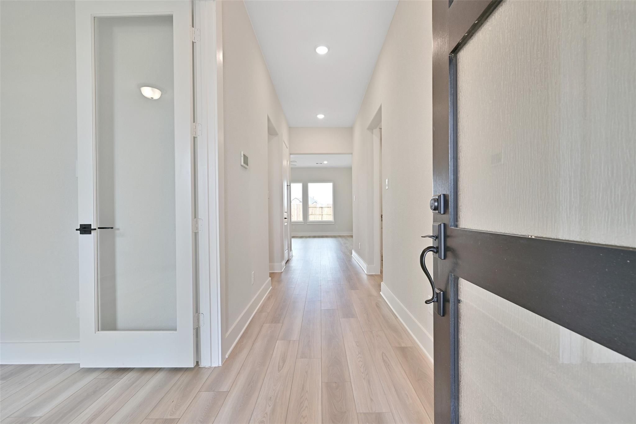 Spacious hallway with light wood floors, frosted glass doors, and recessed lighting in Davidson Homes The Edward C, Lago Mar, Texas City