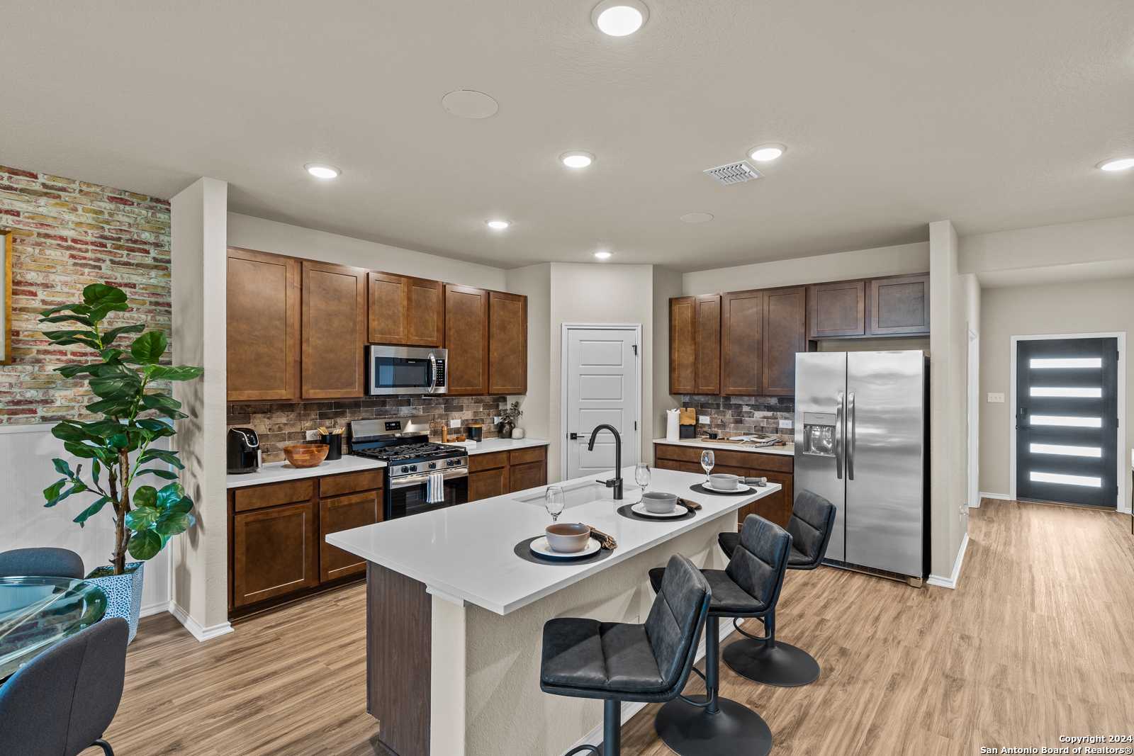 Modern kitchen with dark wood cabinets, white island, stainless appliances, exposed brick wall in The Douglas F by Davidson Homes, Bricewood, San Antonio
