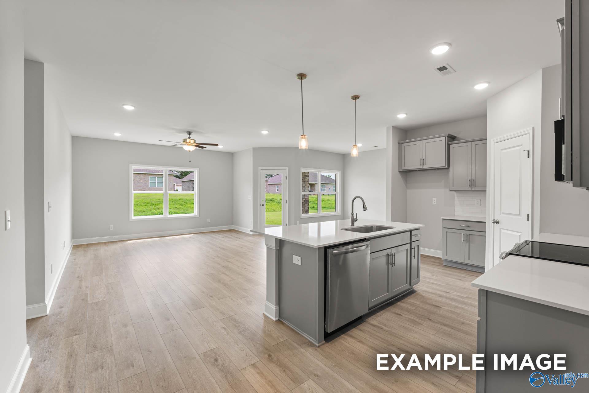 Modern open-concept kitchen with gray island, stainless sink, and hardwood floors overlooking backyard in The Daphne 4-bedroom home, Hazel Green, Alabama