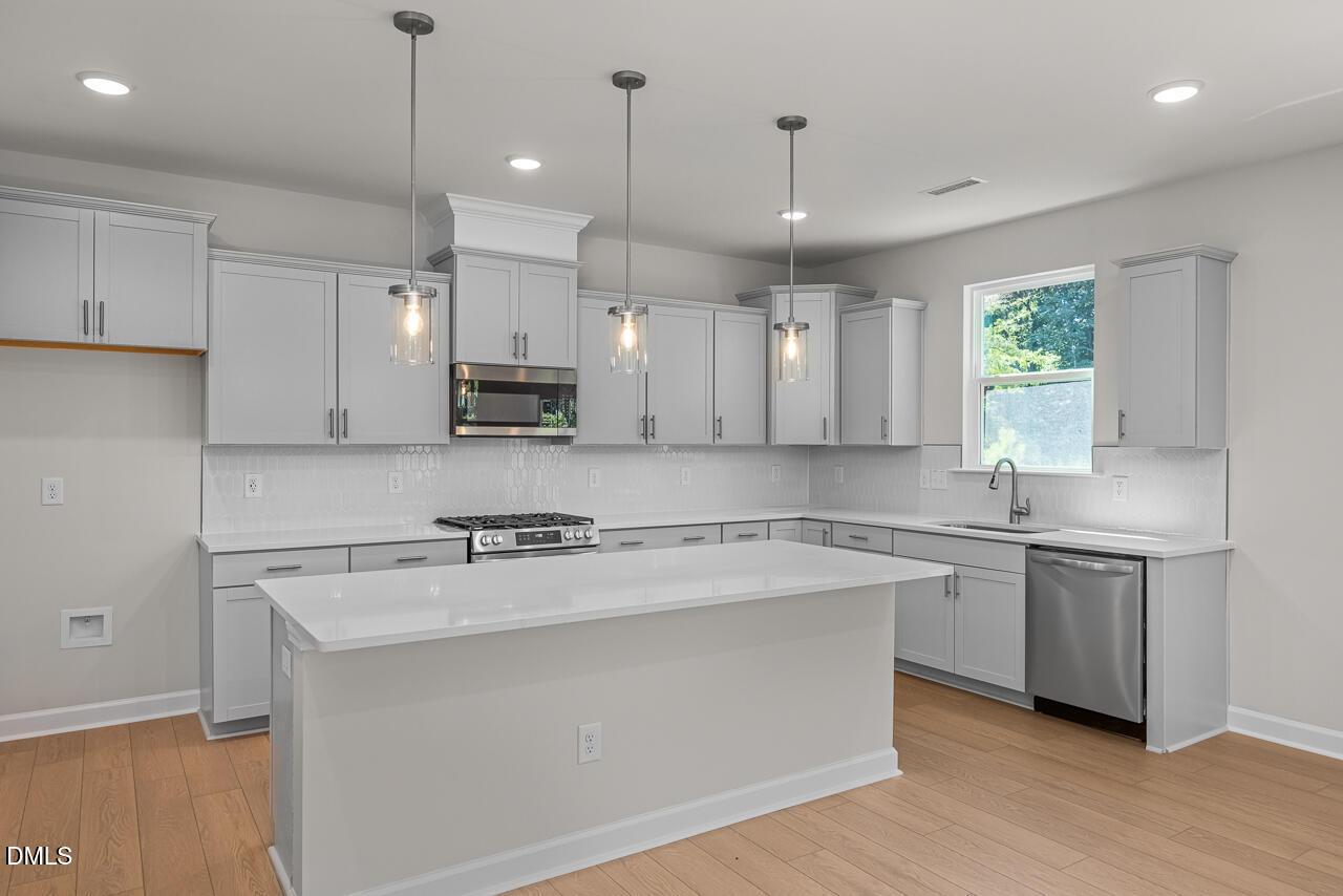 Modern kitchen with gray shaker cabinets, white quartz island, pendant lights, and stainless appliances in Davidson Homes Hickory II C, Aberdeen NC