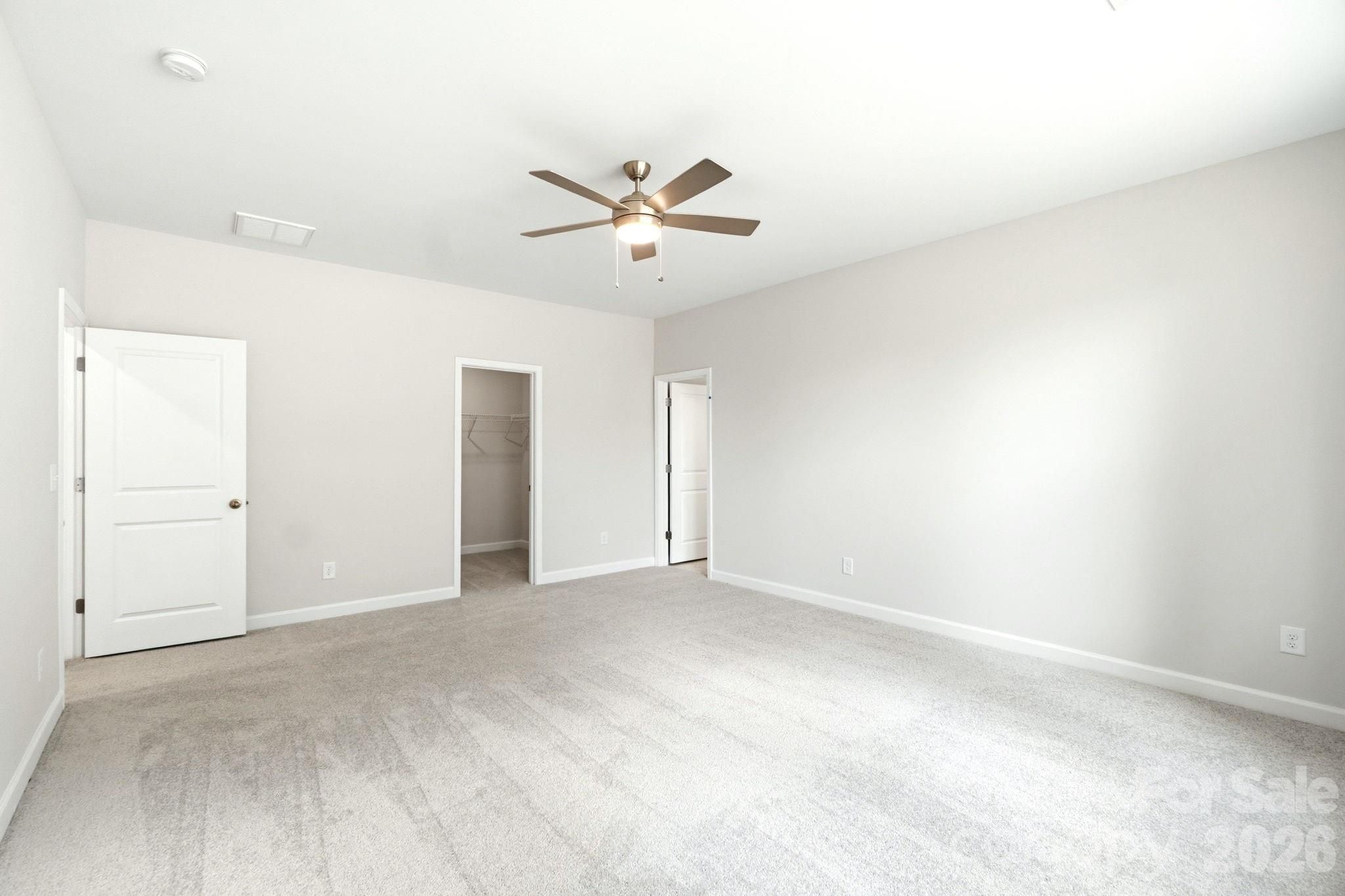 Spacious bedroom with ceiling fan, neutral carpet, and walk-in closet in The Magnolia B floor plan, Windgate, Mooresville.