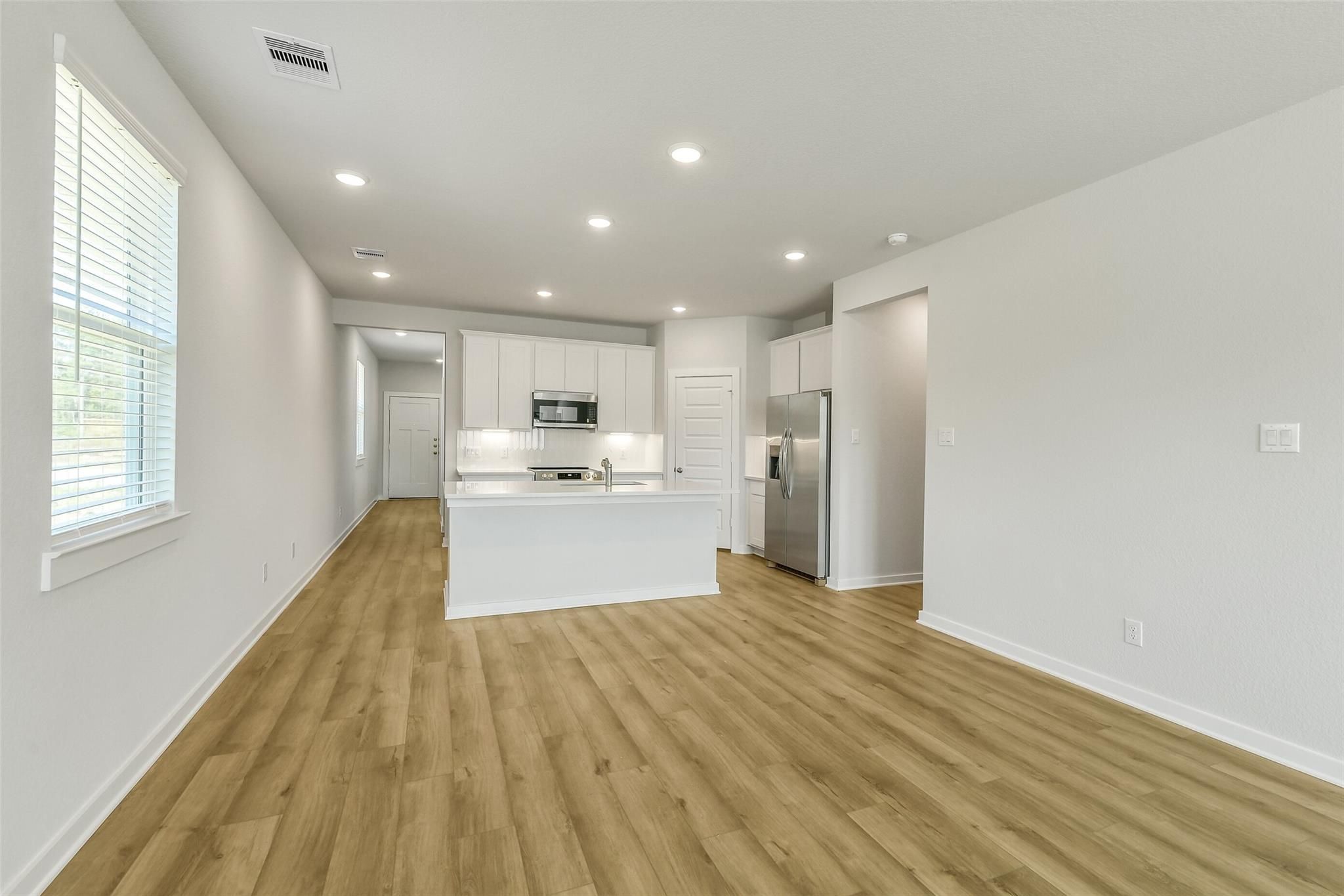Modern open-concept kitchen with white island, stainless appliances, oak floors in Davidson Homes The San Marcos E, Cleveland, Texas