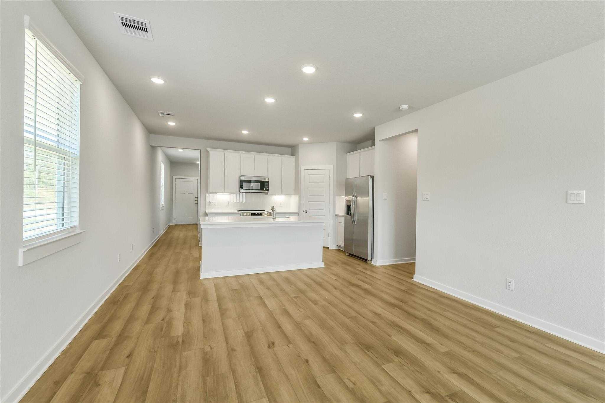 Modern open-concept kitchen with white island, stainless appliances, oak floors in Davidson Homes The San Marcos E, Cleveland, Texas