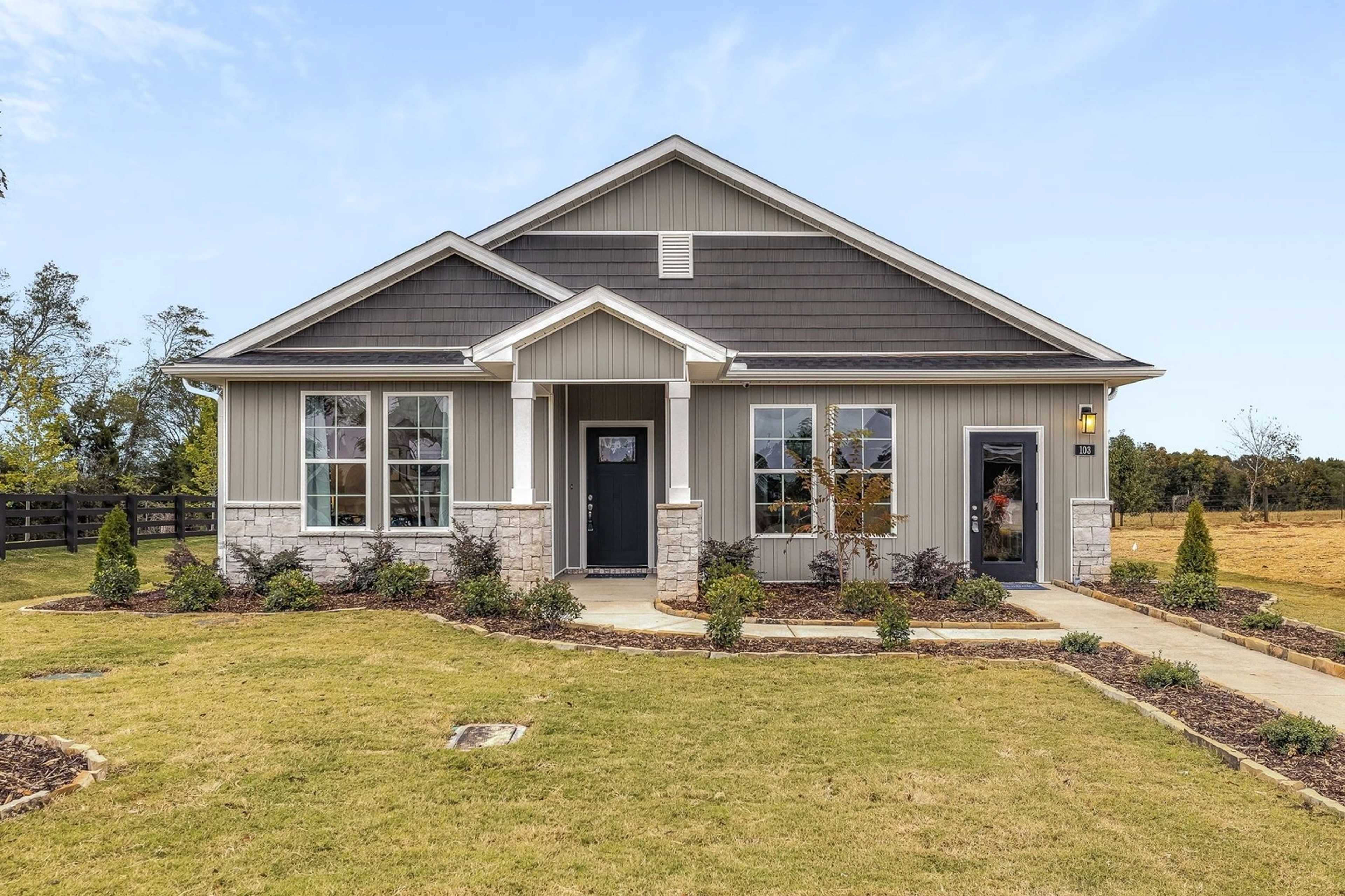 Charming gray craftsman home exterior at Carroll Green in Harvest Alabama with covered porch stone accents and lush yard