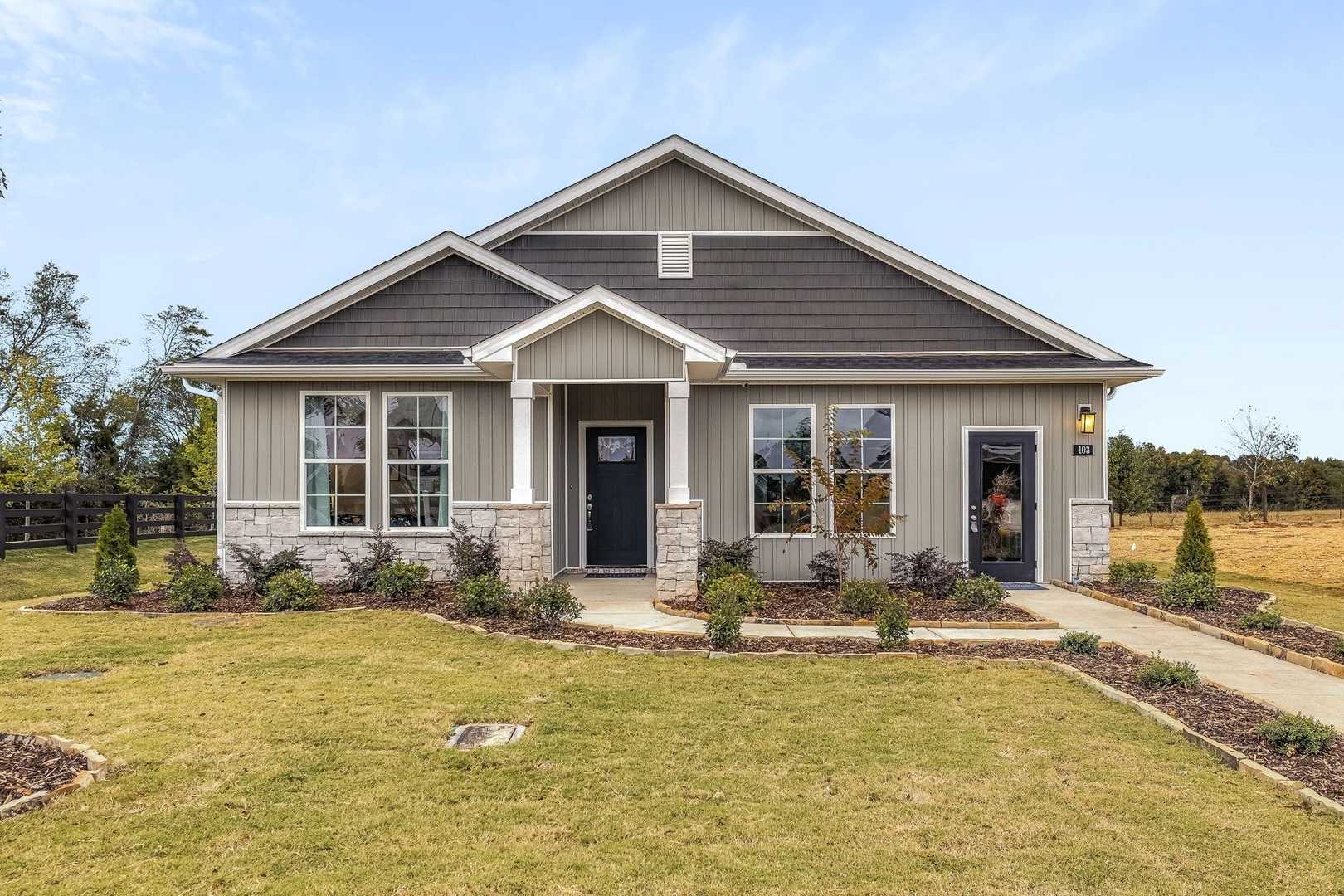 Charming gray craftsman home exterior at Carroll Green in Harvest Alabama with covered porch stone accents and lush yard