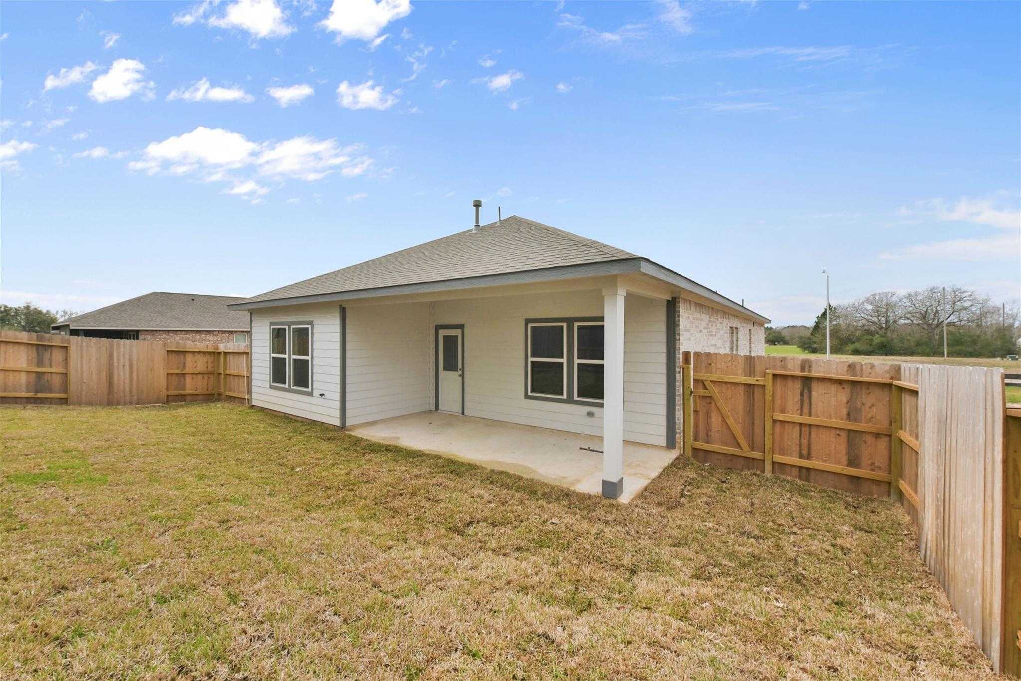Single-story Laguna B home back exterior with covered porch, white siding, fenced grassy yard in Windmill Estates, Magnolia, Texas