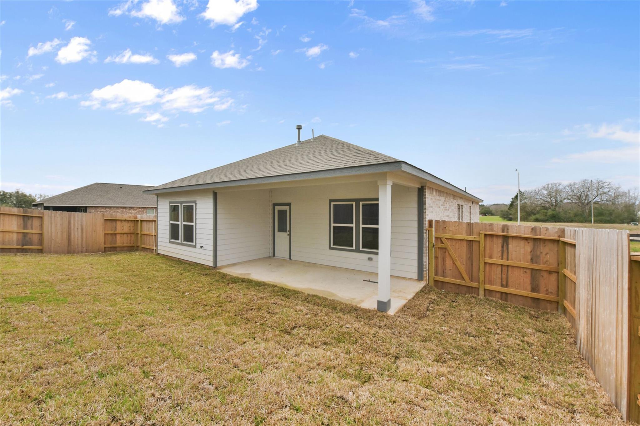 Single-story Laguna B home back exterior with covered porch, white siding, fenced grassy yard in Windmill Estates, Magnolia, Texas