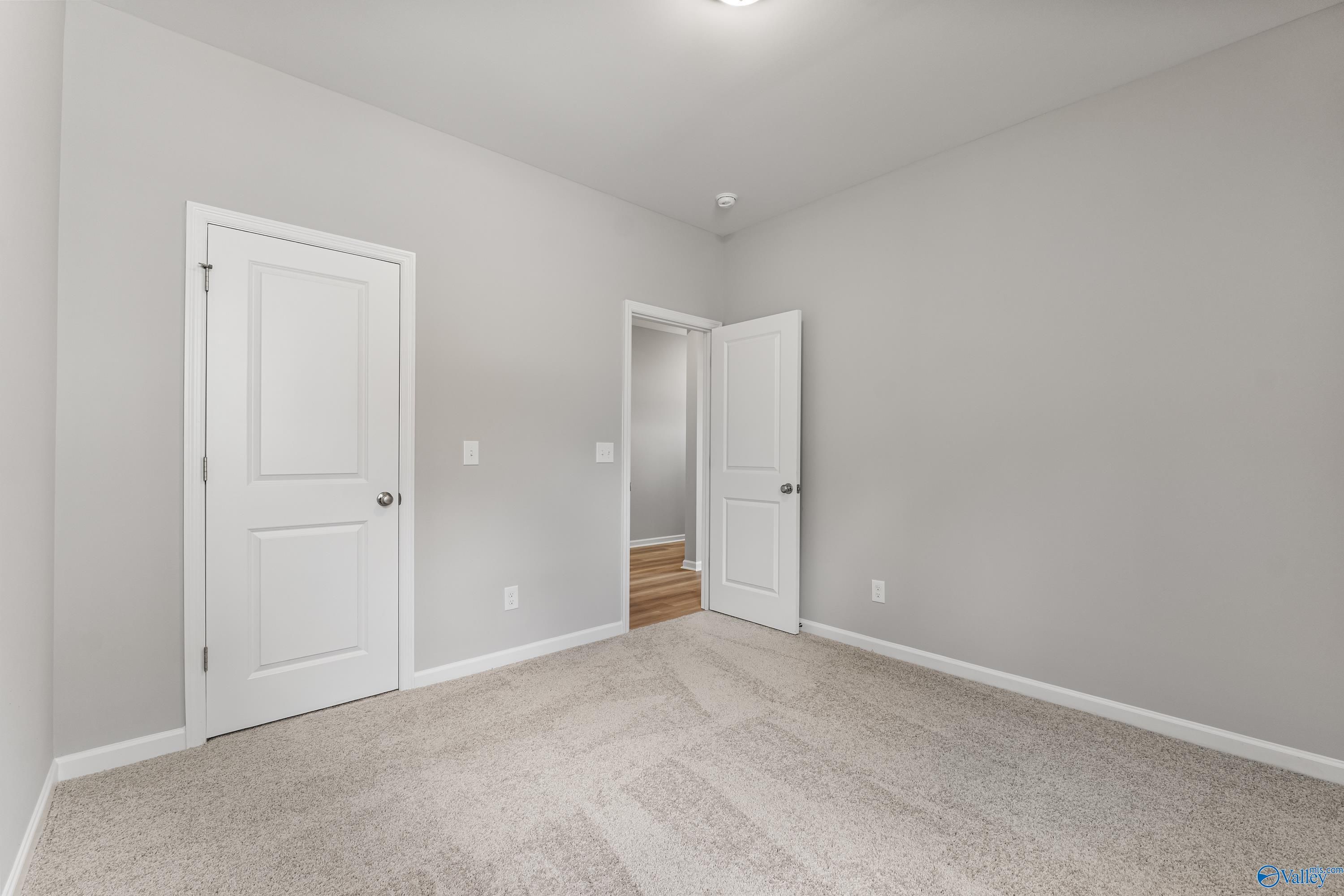 Spacious secondary bedroom with light gray walls, white doors, and beige carpet in Davidson Homes The Phoenix, Hazel Green, Alabama