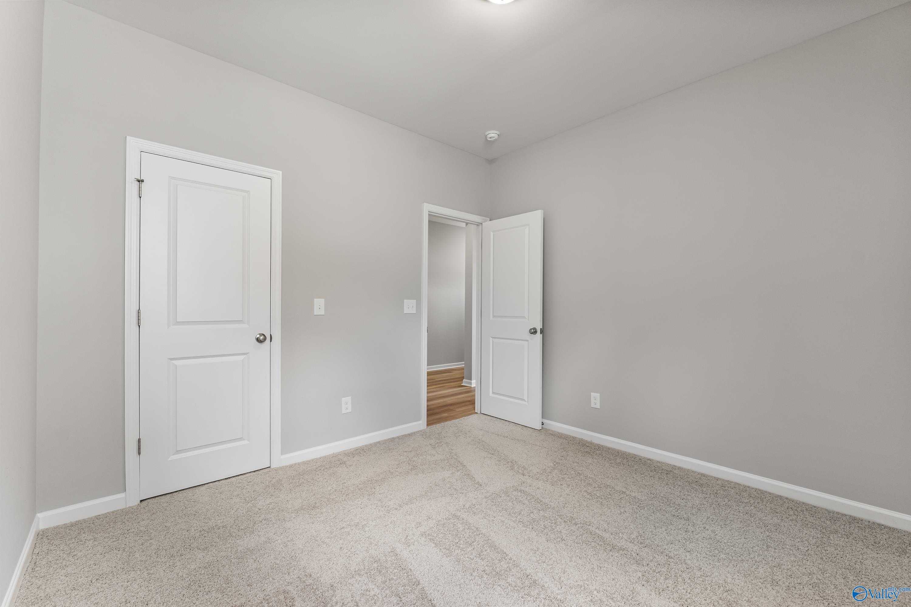 Spacious secondary bedroom with light gray walls, beige carpet, and open bathroom door in The Phoenix, Davidson Homes, Hazel Green, AL