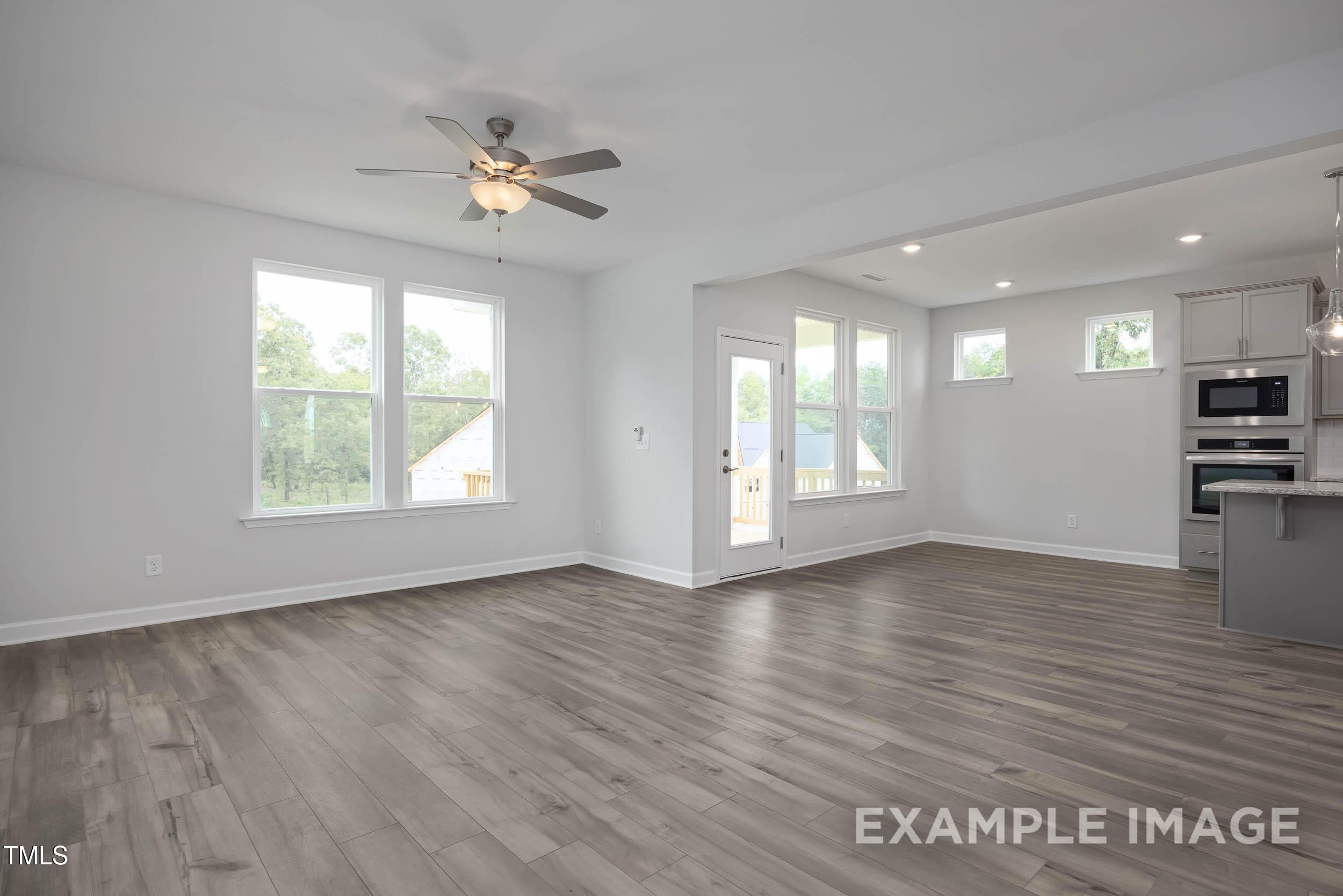 Open-concept living area with hardwood floors, large windows, ceiling fan, and modern gray kitchen in Davidson Homes The Willow E, Angier, NC
