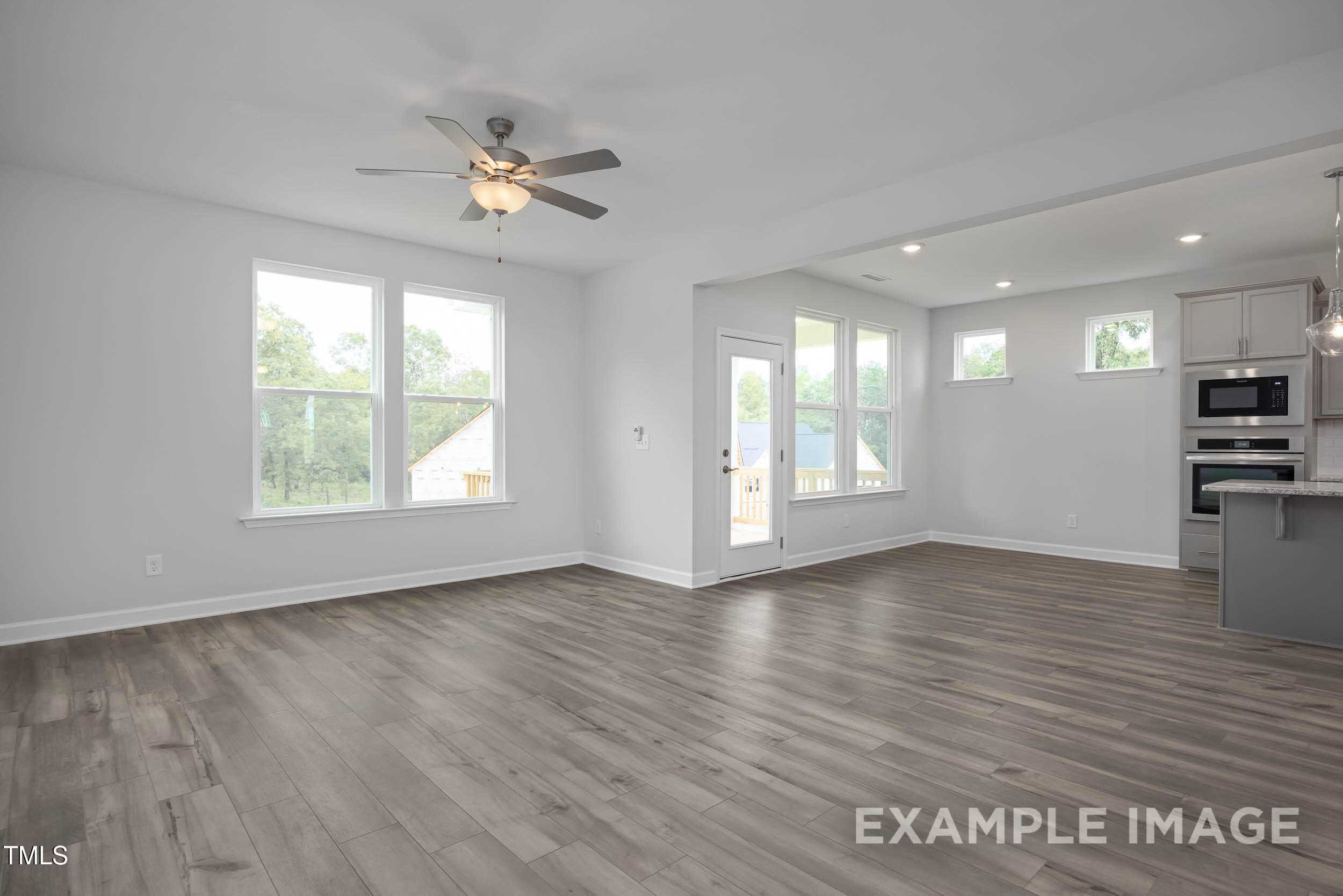 Open-concept living area with hardwood floors, large windows, ceiling fan, and modern gray kitchen in Davidson Homes The Willow E, Angier, NC