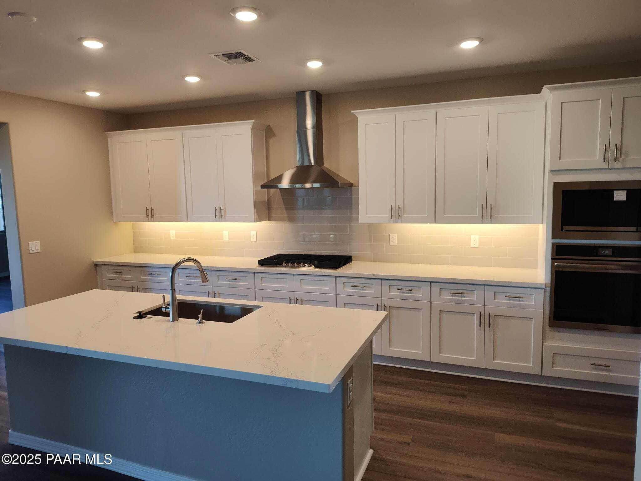 Modern white cabinet kitchen with quartz island, stainless range hood, oven, and cooktop in Davidson Homes The Inspiration A, Prescott Valley
