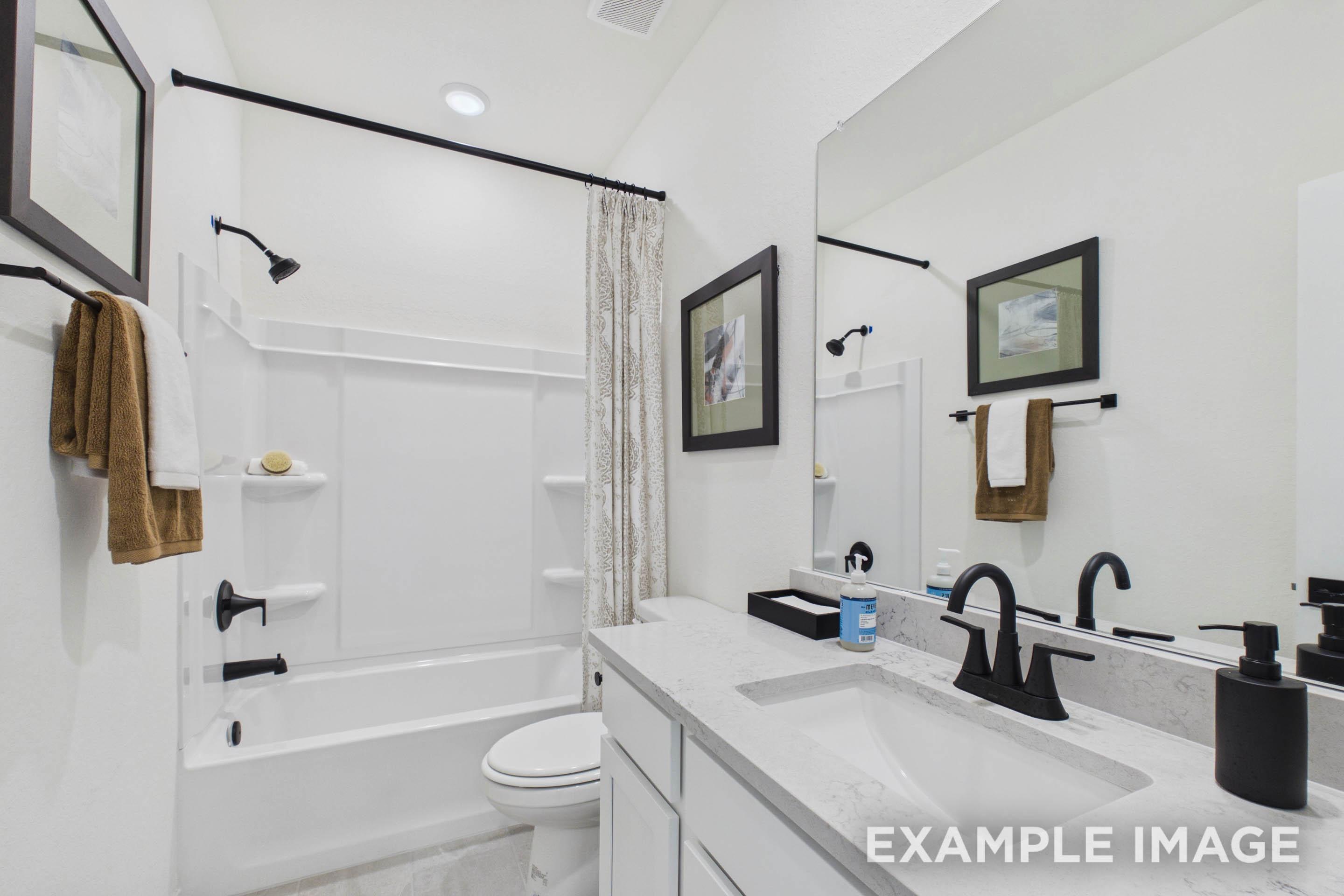 Modern bathroom in The Laurel G featuring a white vanity, stone countertop, and combination shower and tub.