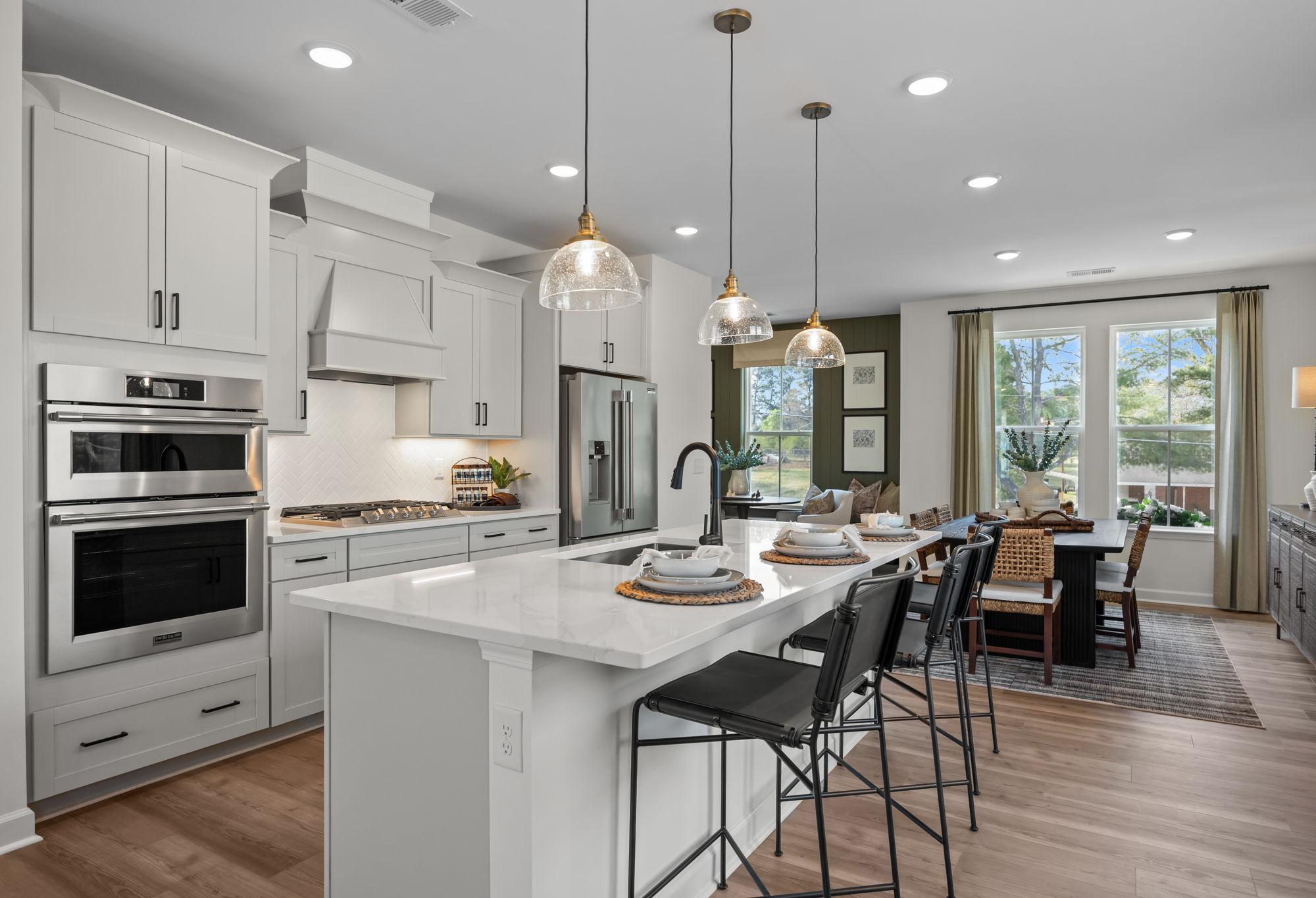 Modern kitchen in The Mitchell by Davidson Homes featuring a large quartz island, stainless appliances, and dining area.