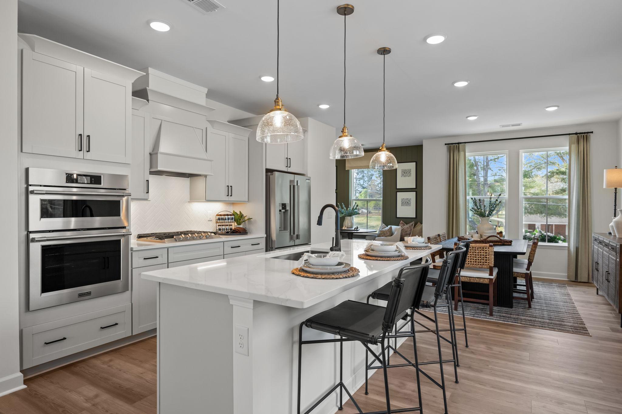 Modern kitchen with white cabinets, quartz island, stainless appliances, and dining area at Camden Park in Knightdale NC by Davidson Homes