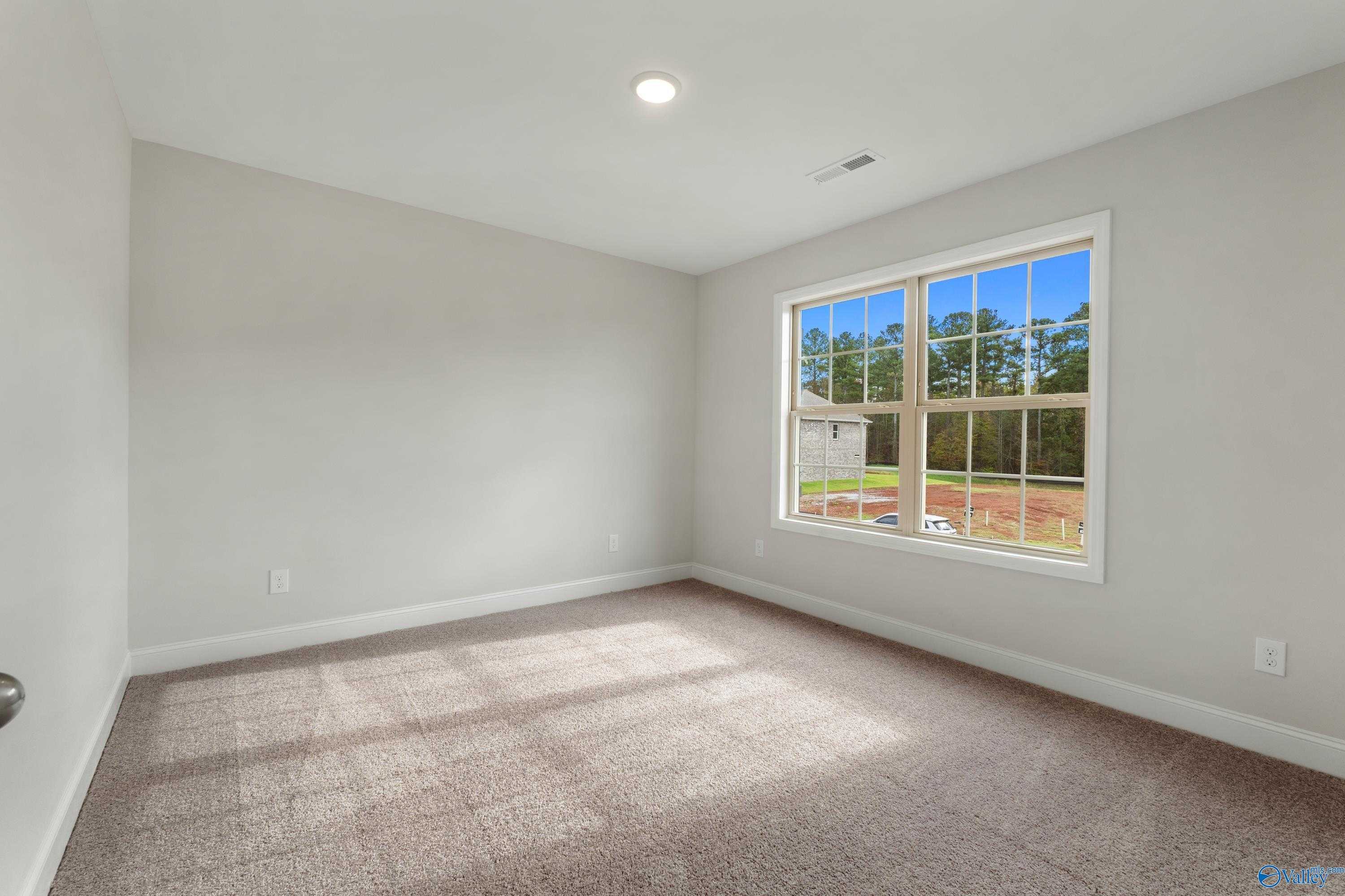 Bright empty bedroom with gray walls, carpet flooring, and large window overlooking trees in Davidson Homes The Chelsea C, Harvest AL