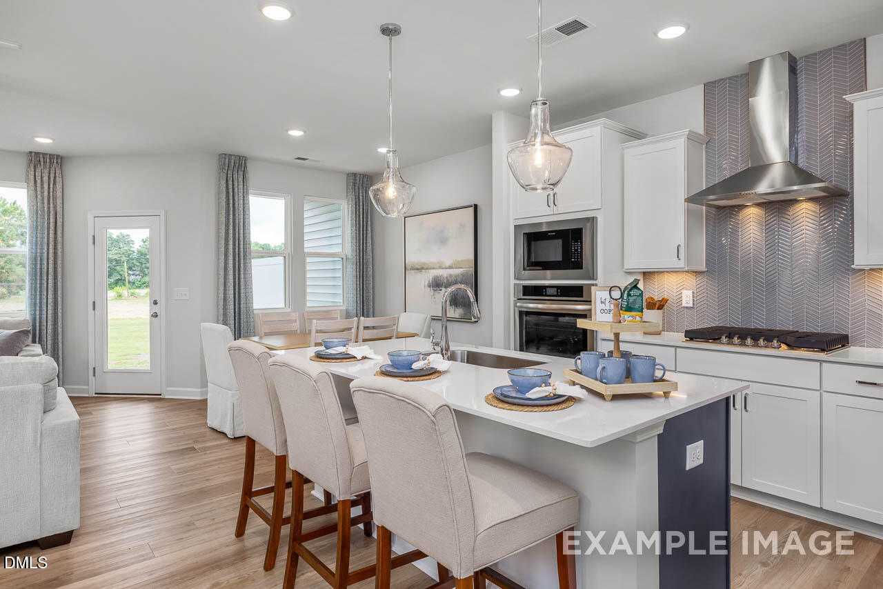 Modern open-concept kitchen with white cabinets, stainless steel appliances, island bar, and adjacent dining area in Davidson Homes The Graham, Fuquay-Varina