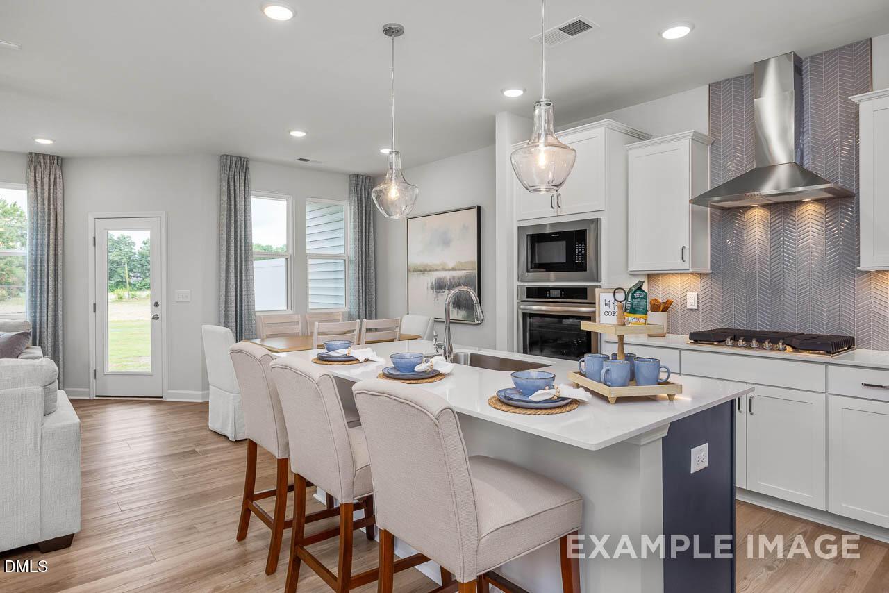 Modern open-concept kitchen with white cabinets, stainless steel appliances, subway tile backsplash, and breakfast island in The Graham floor plan, Fuquay-Varina, NC