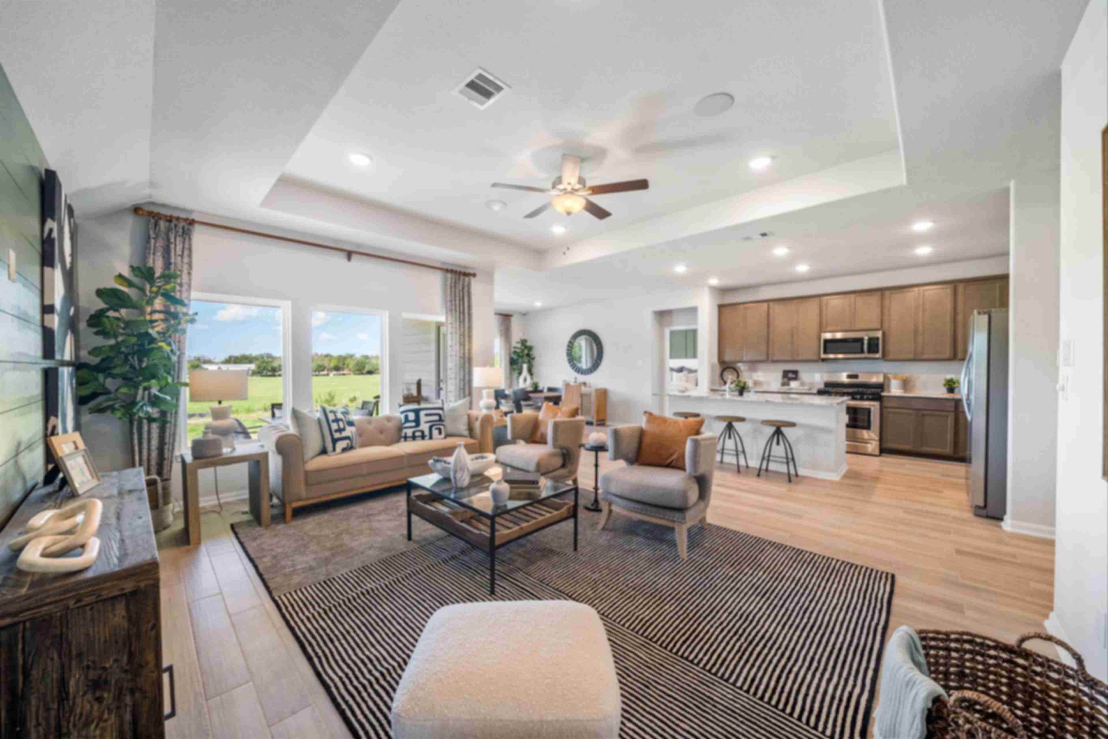 Open-concept living room and kitchen at Windmill Estates in Magnolia TX with hardwood floors, ceiling fan, and large windows