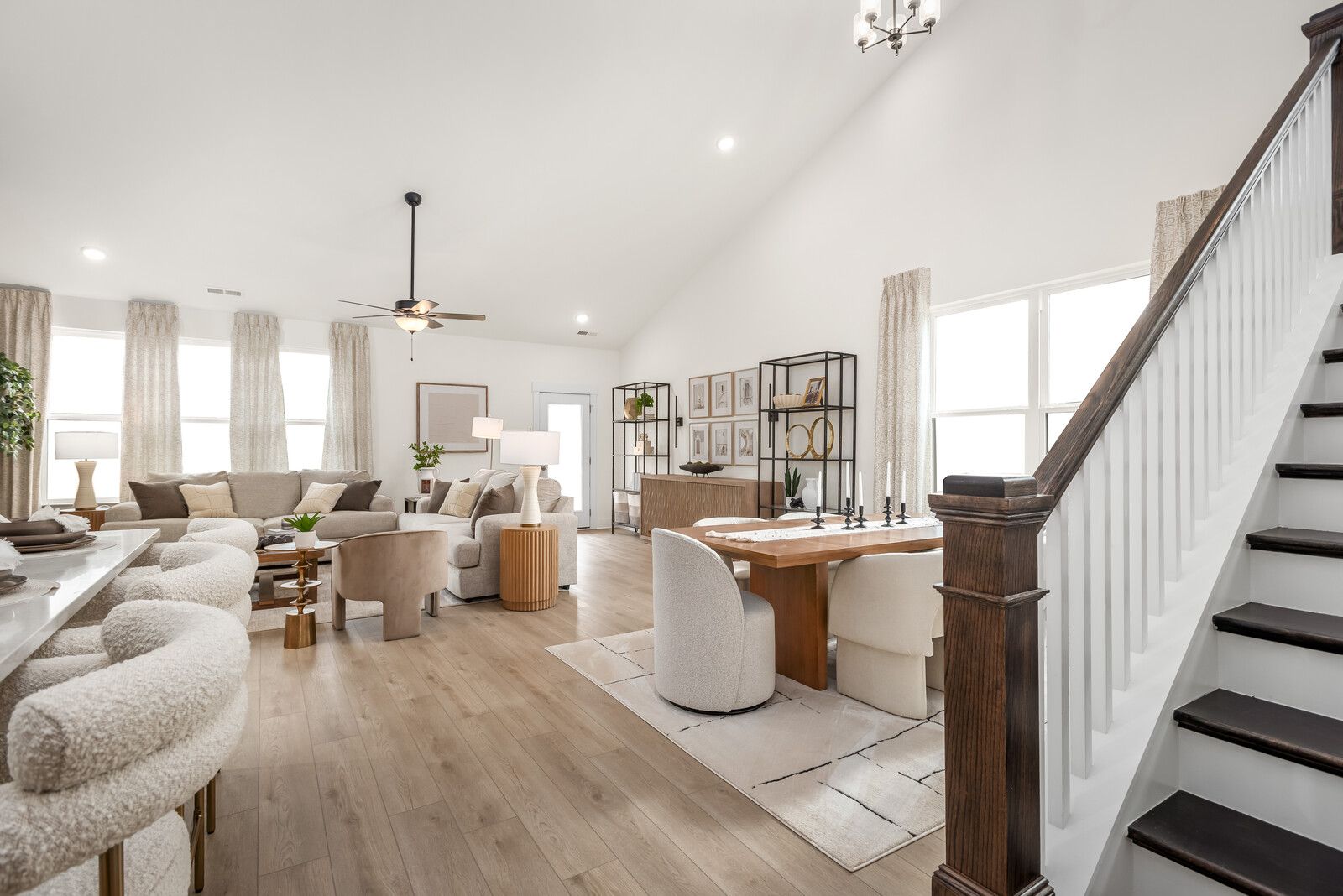 Spacious open-concept living and dining area in The Ridgeport E with modern white furniture, wooden staircase, vaulted ceiling, and large windows
