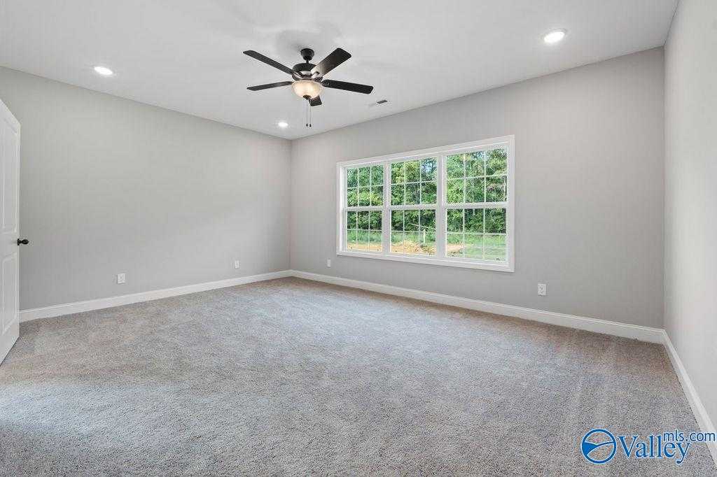 Spacious bedroom with gray carpet, ceiling fan, and large windows to lush trees in Davidson Homes The Montgomery B, Hartselle, AL