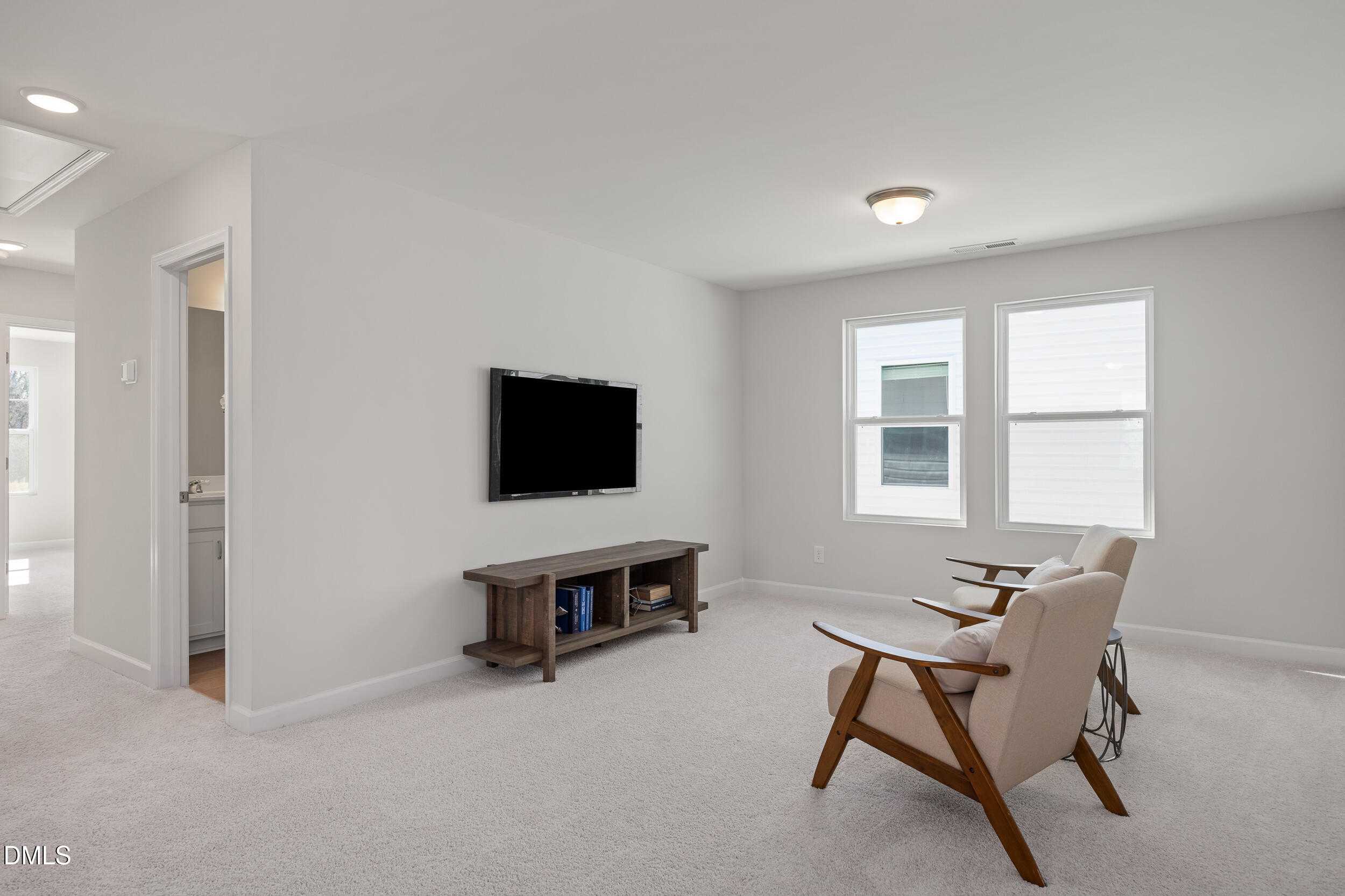 Cozy upstairs loft with wall-mounted TV, wooden media console, armchairs, and large windows in Davidson Homes The Preston C, Lillington, NC
